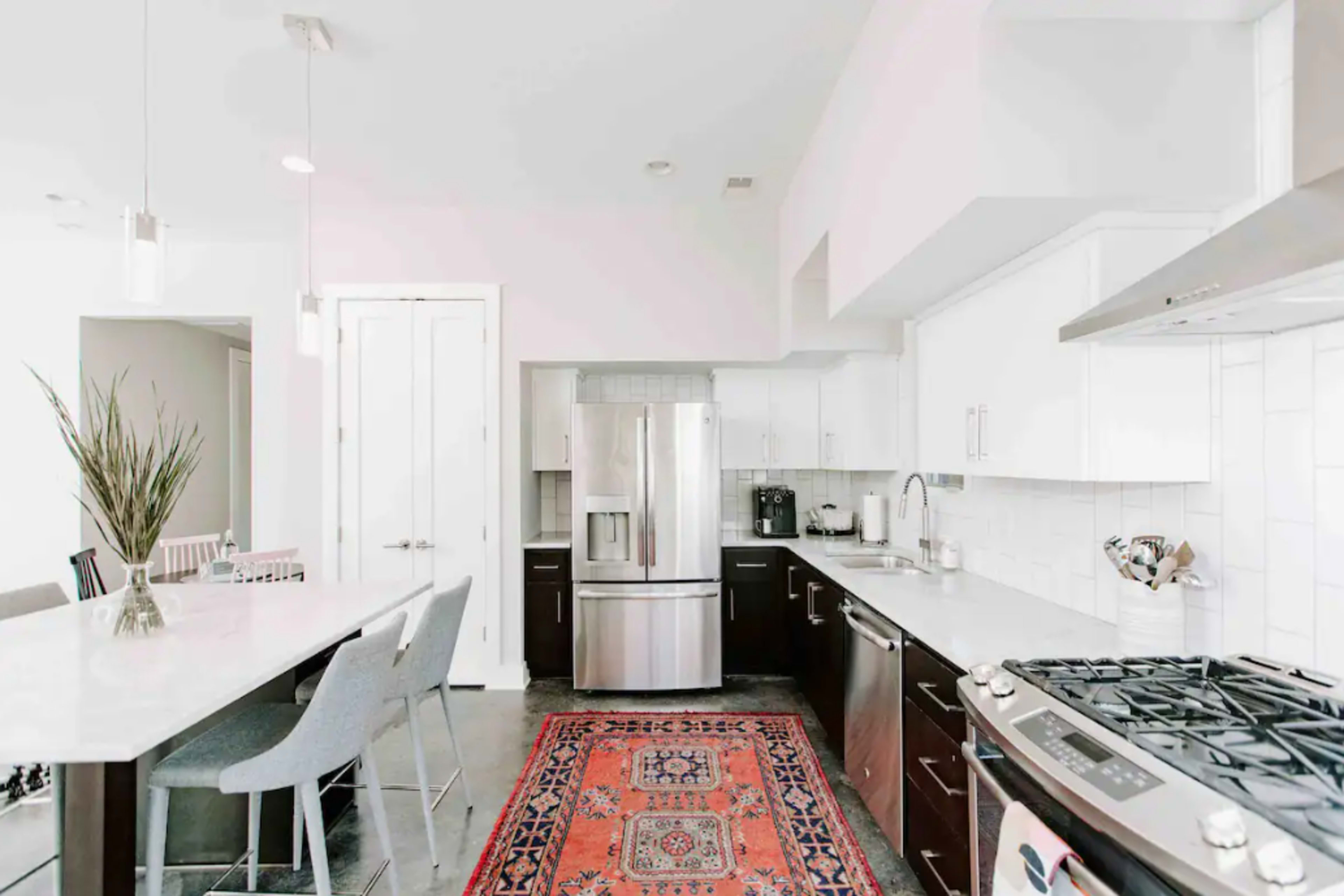 A modern kitchen features stainless steel appliances, white cabinetry, and a central island with bar seating, alongside a traditional patterned rug.