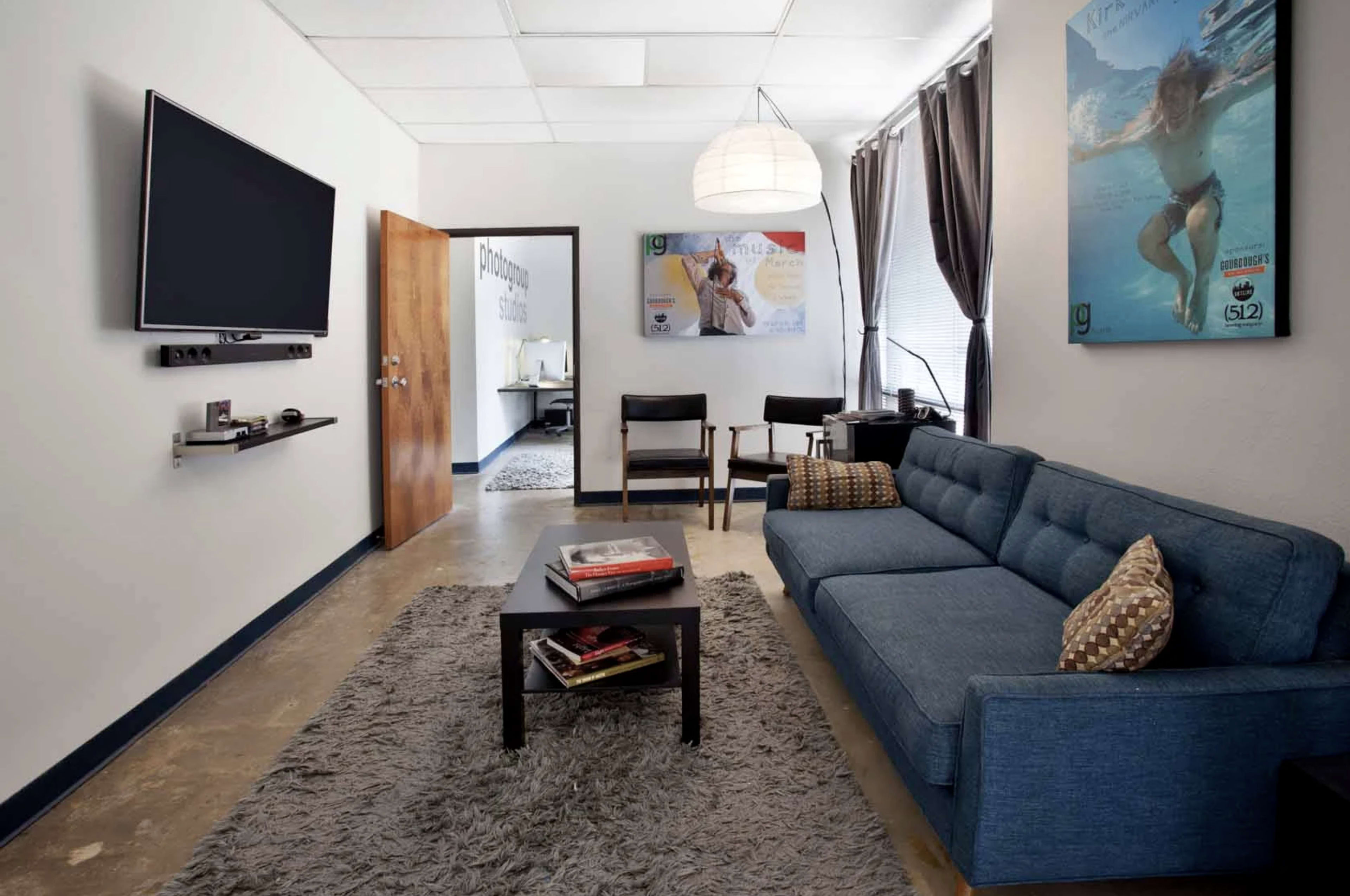 A modern living room featuring a blue sofa, a coffee table on a rug, a mounted TV, and a doorway leading to another room.