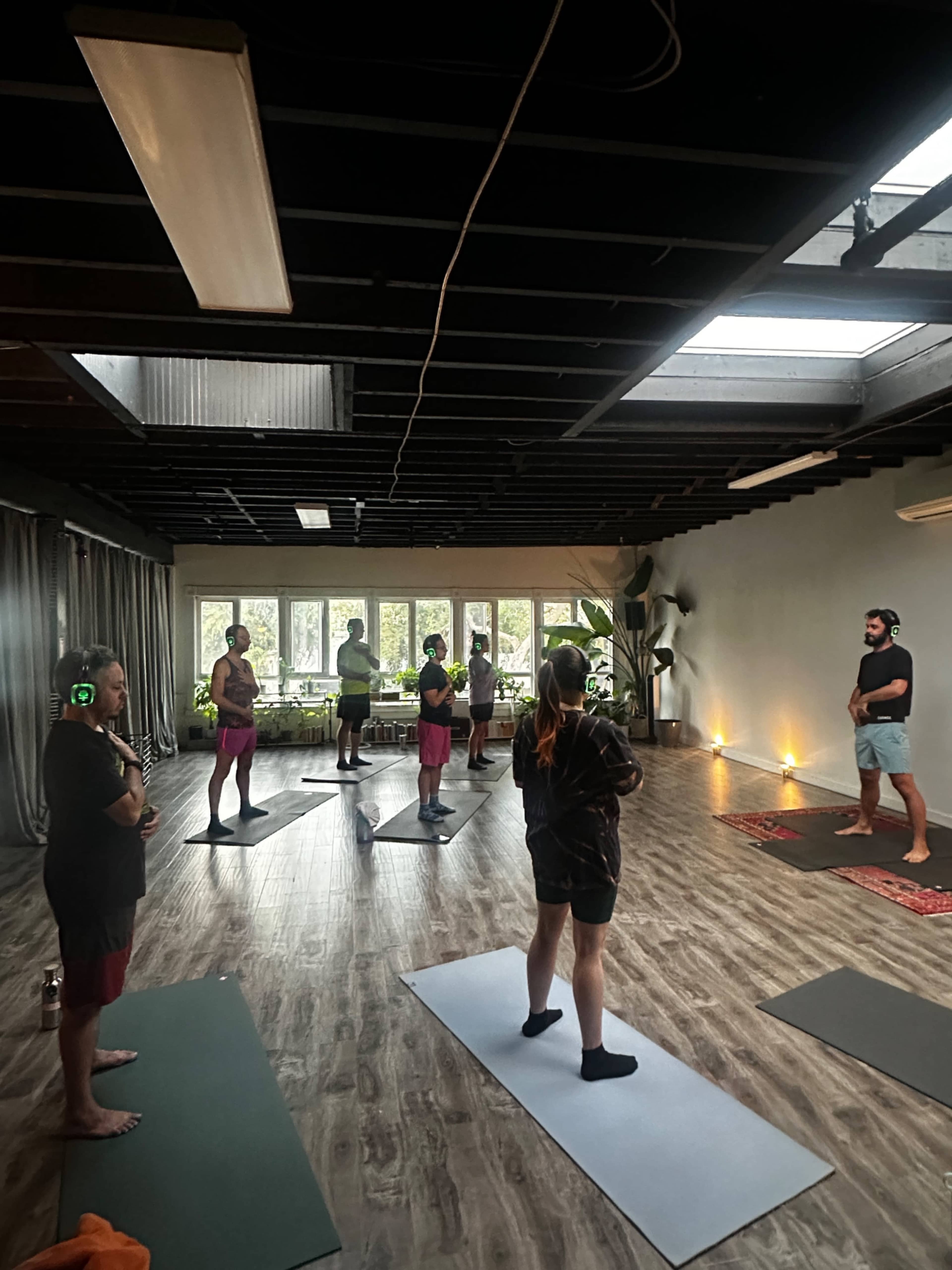 A group of individuals participates in a yoga class inside a spacious studio with natural light filtering through large windows.