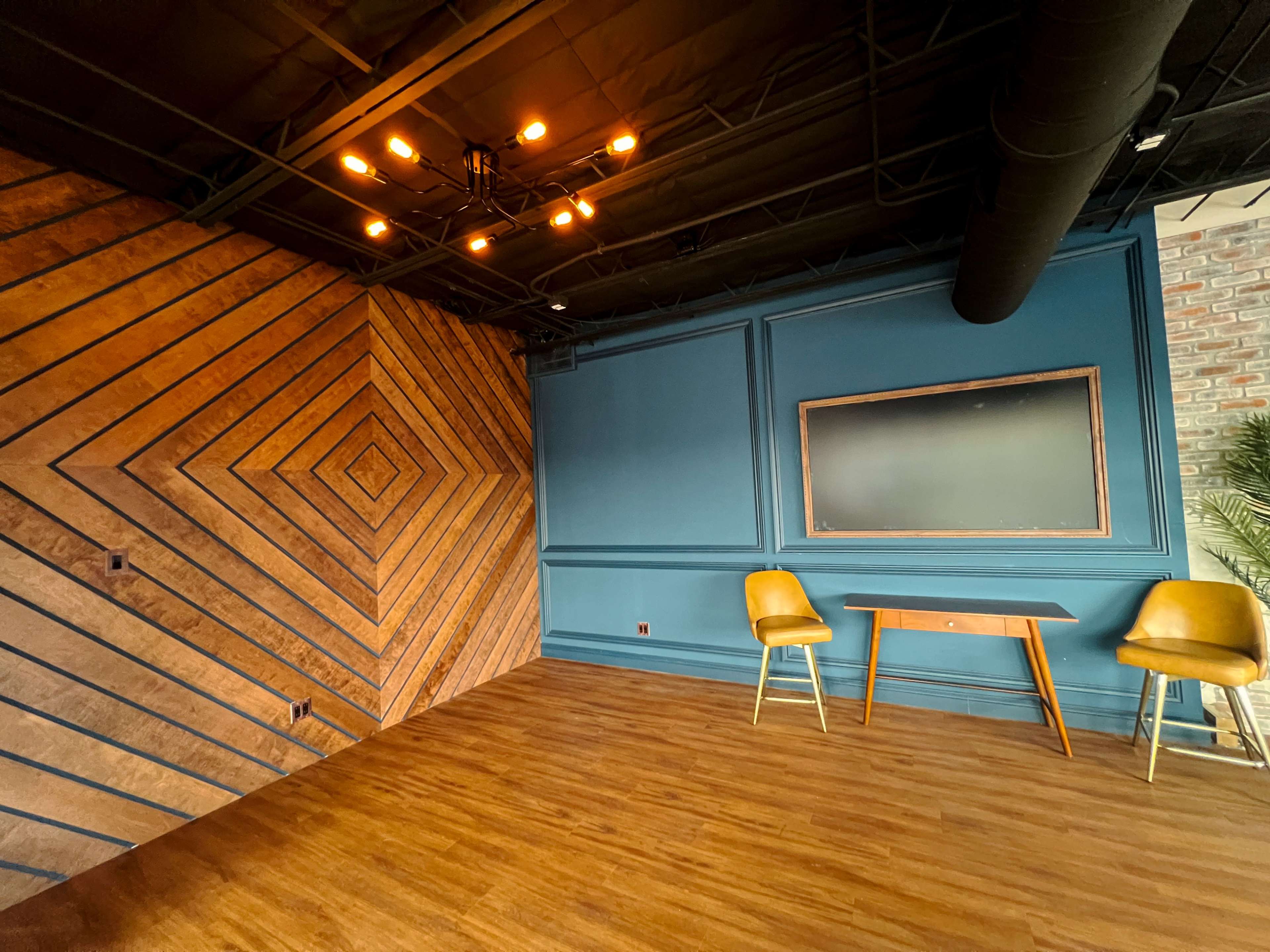 The image shows a modern interior space featuring a patterned wooden wall, a blue accent wall, a wooden table, and two yellow chairs.