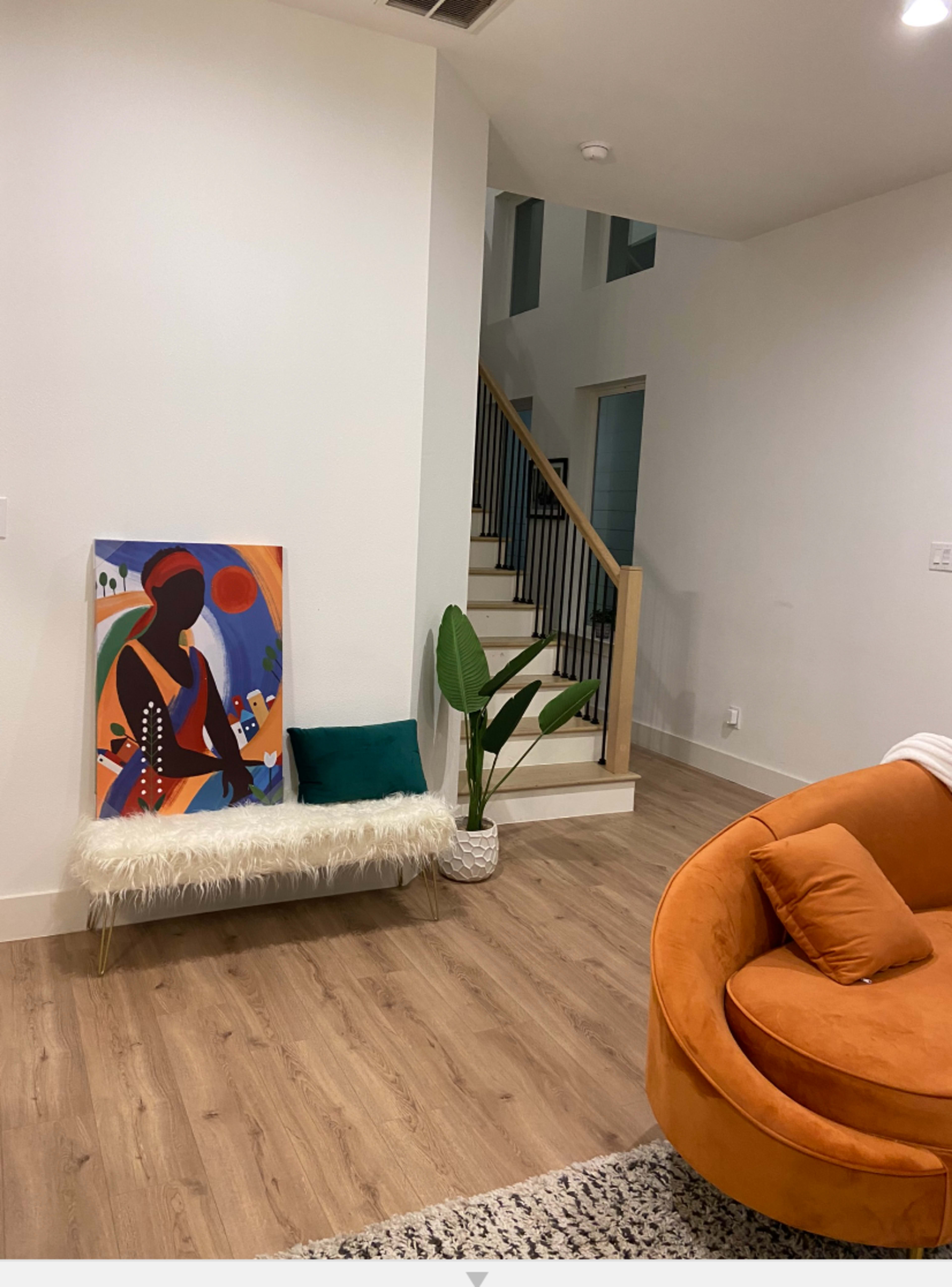 A modern living space featuring a colorful painting on a bench, a potted plant, and a staircase in the background.