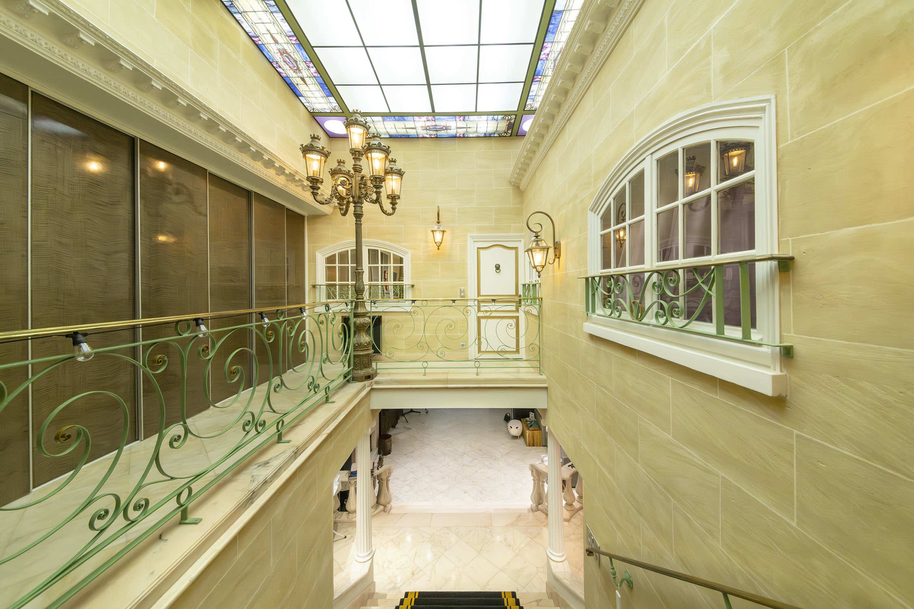 An elegant hallway with a staircase, decorative iron railing, and stained glass ceiling lights.