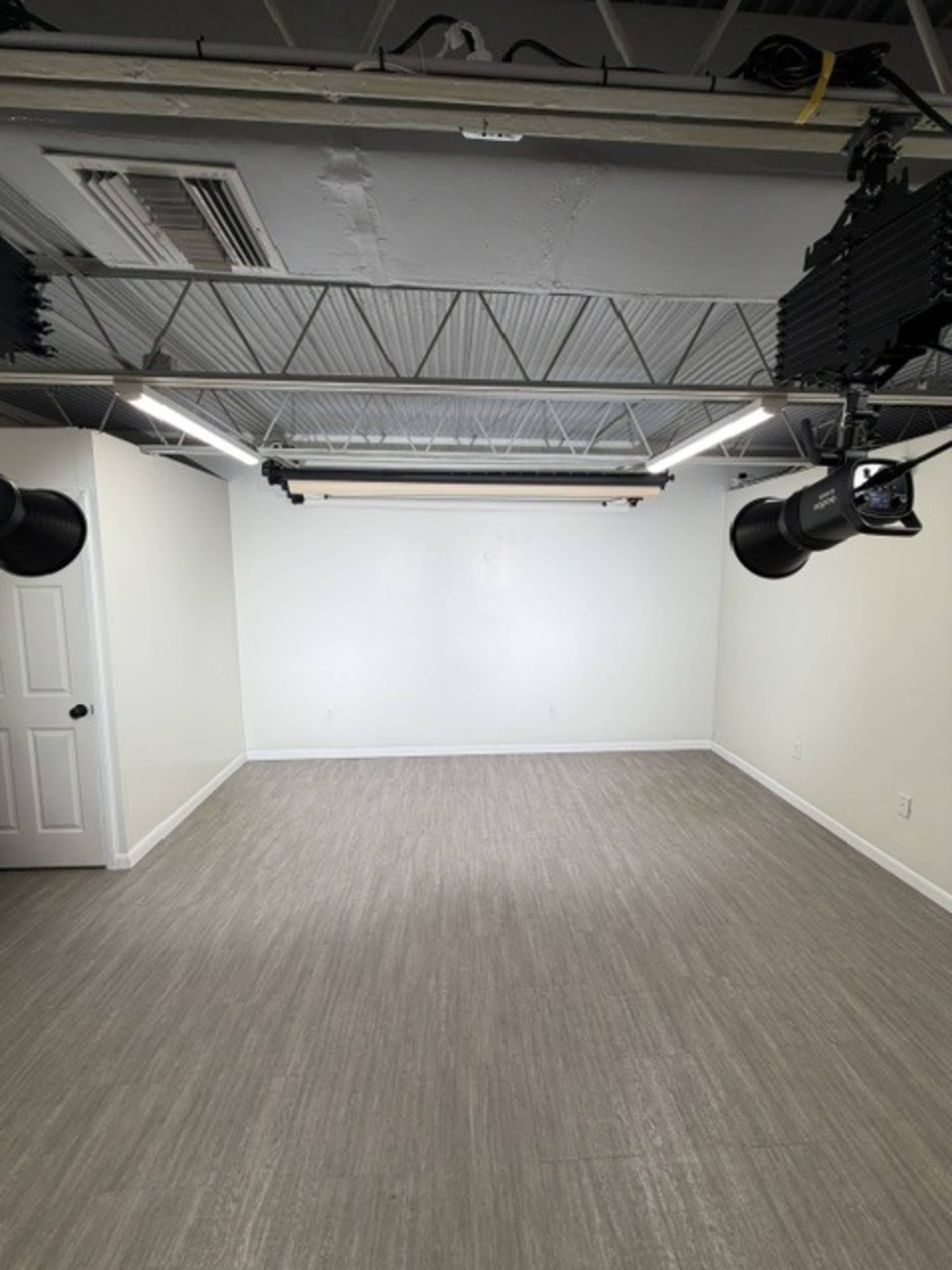 The image shows an empty room with white walls, a smooth gray floor, and ceiling lights installed above.
