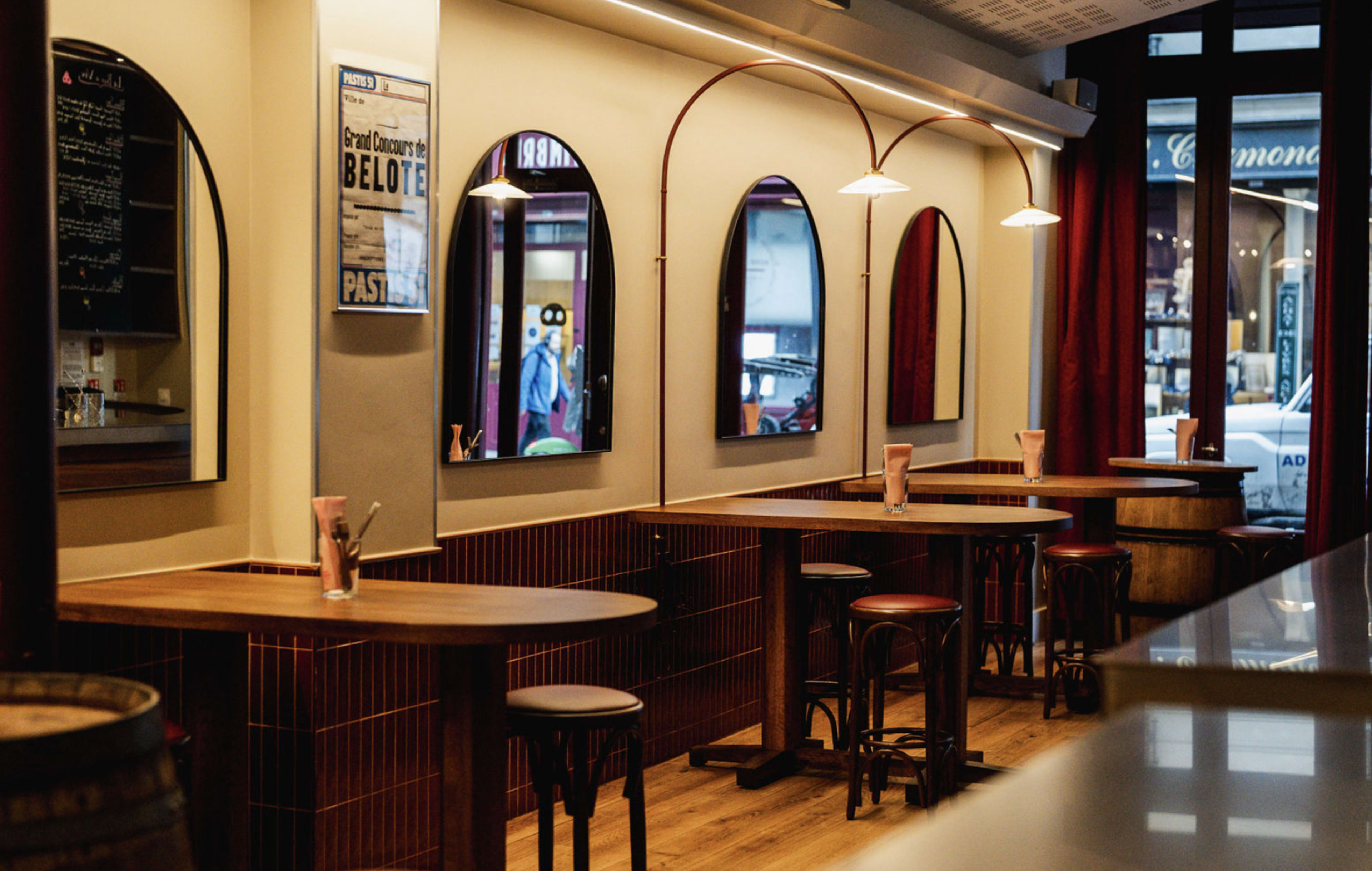 The interior of a café features wooden tables and stools, arched mirrors on the walls, and soft lighting.