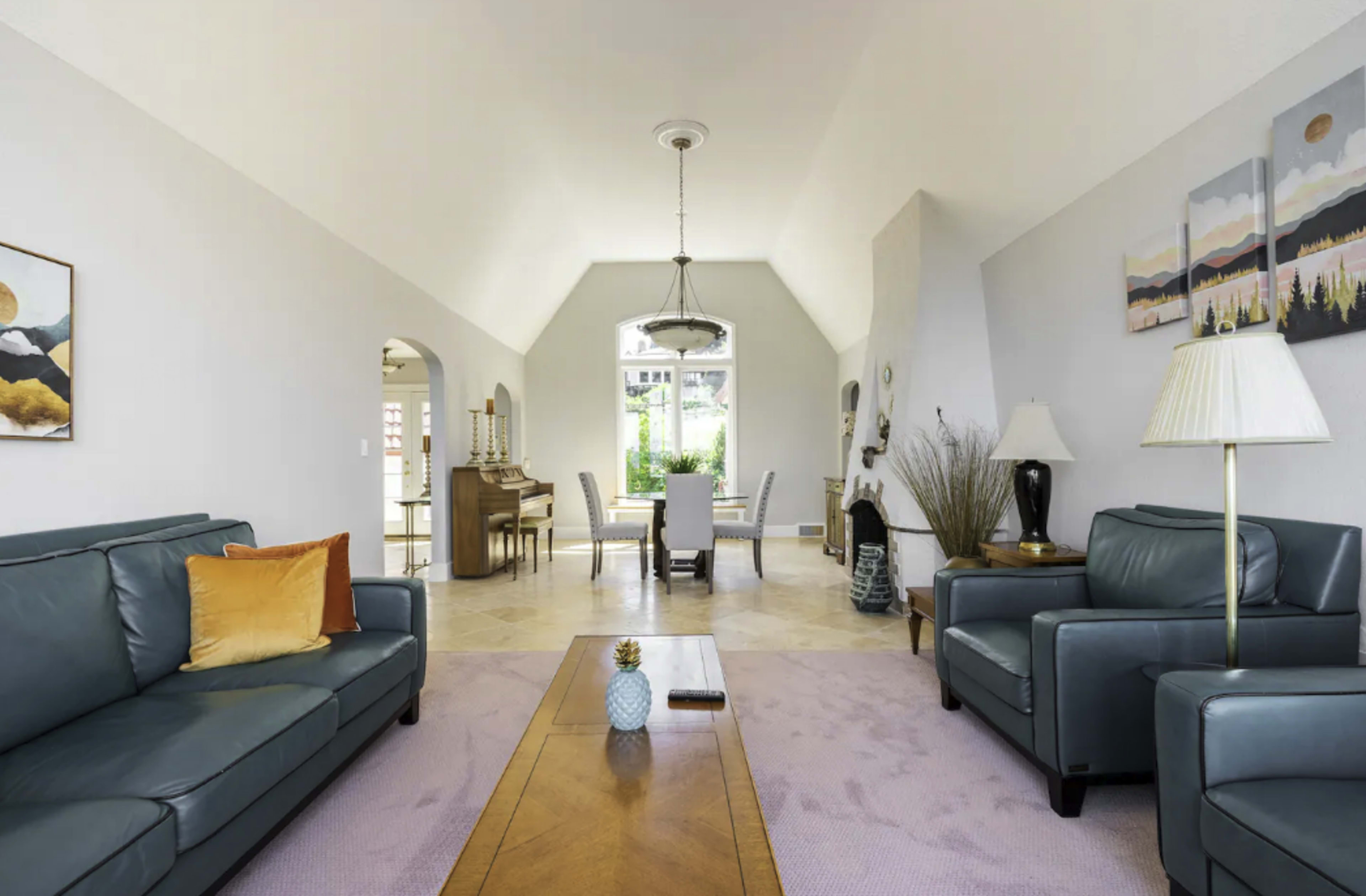 The spacious living room features two leather sofas, a wooden coffee table, and a dining area illuminated by natural light from large windows.