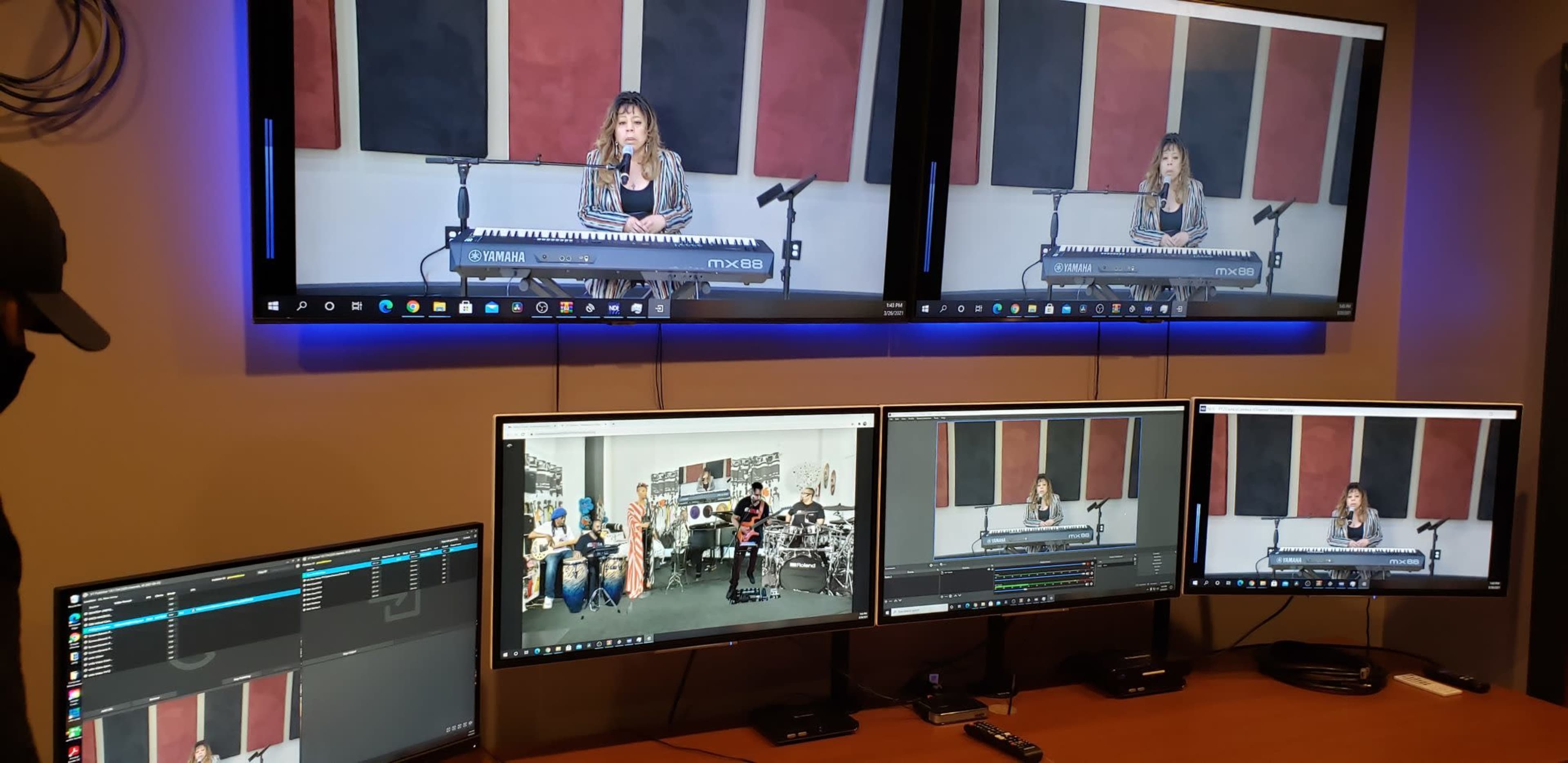 A person is performing on a keyboard in a recording studio, with multiple screens displaying the performance and video editing software.