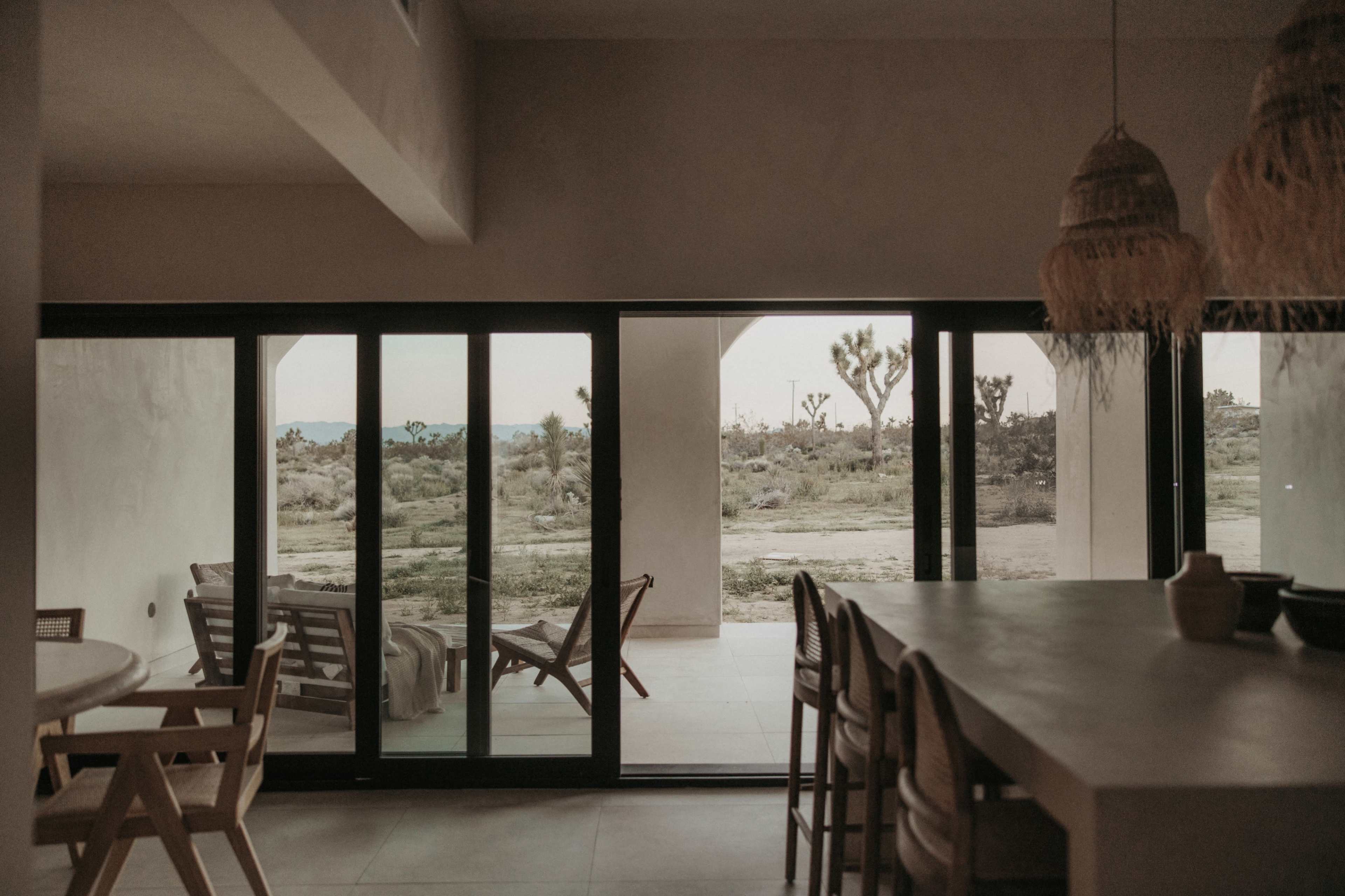 A spacious, modern interior with large glass doors that open to a desert landscape featuring scattered vegetation.