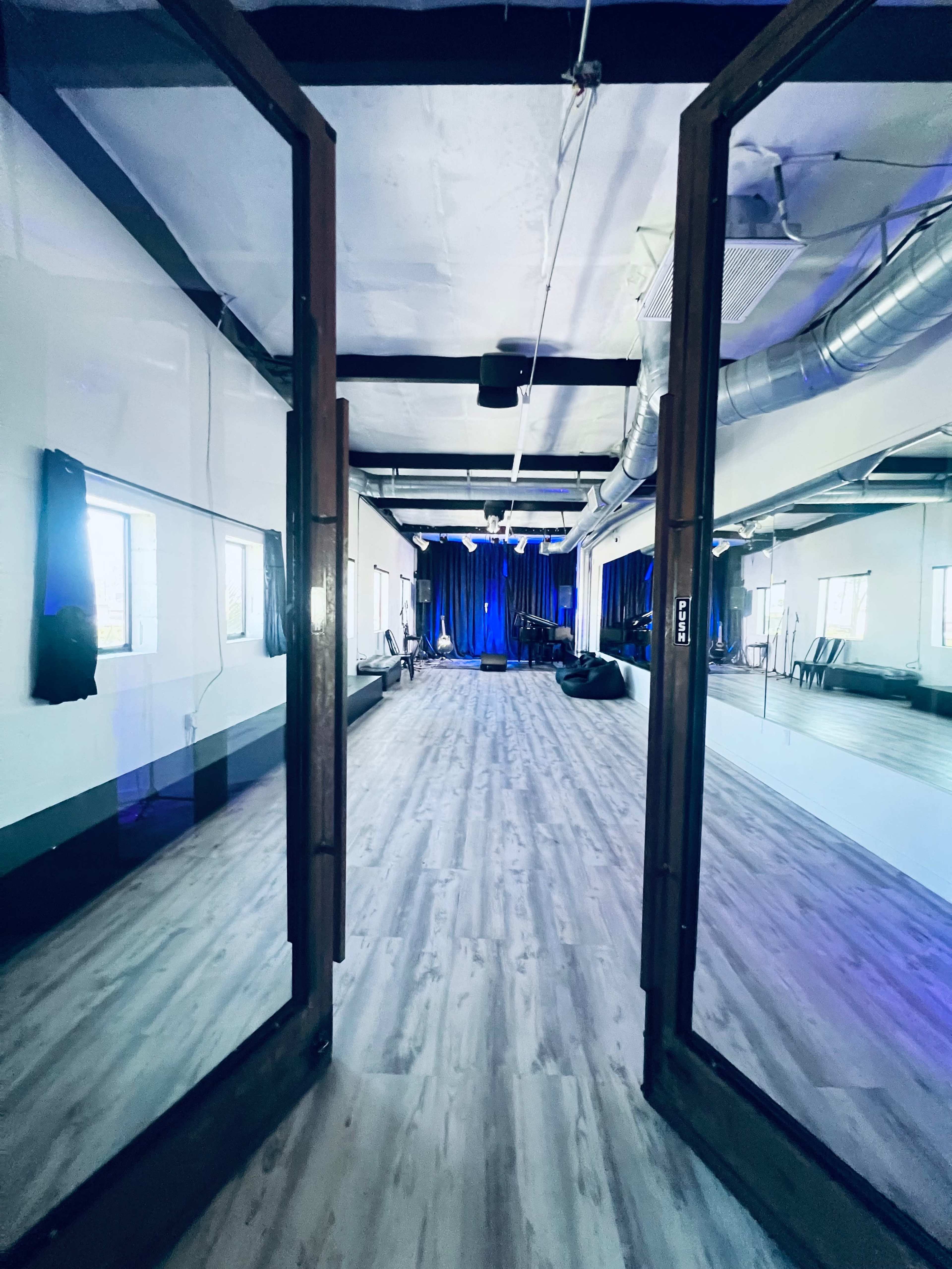 A spacious, mirrored room with a wooden floor and dark curtains in the background, illuminated by blue lighting.