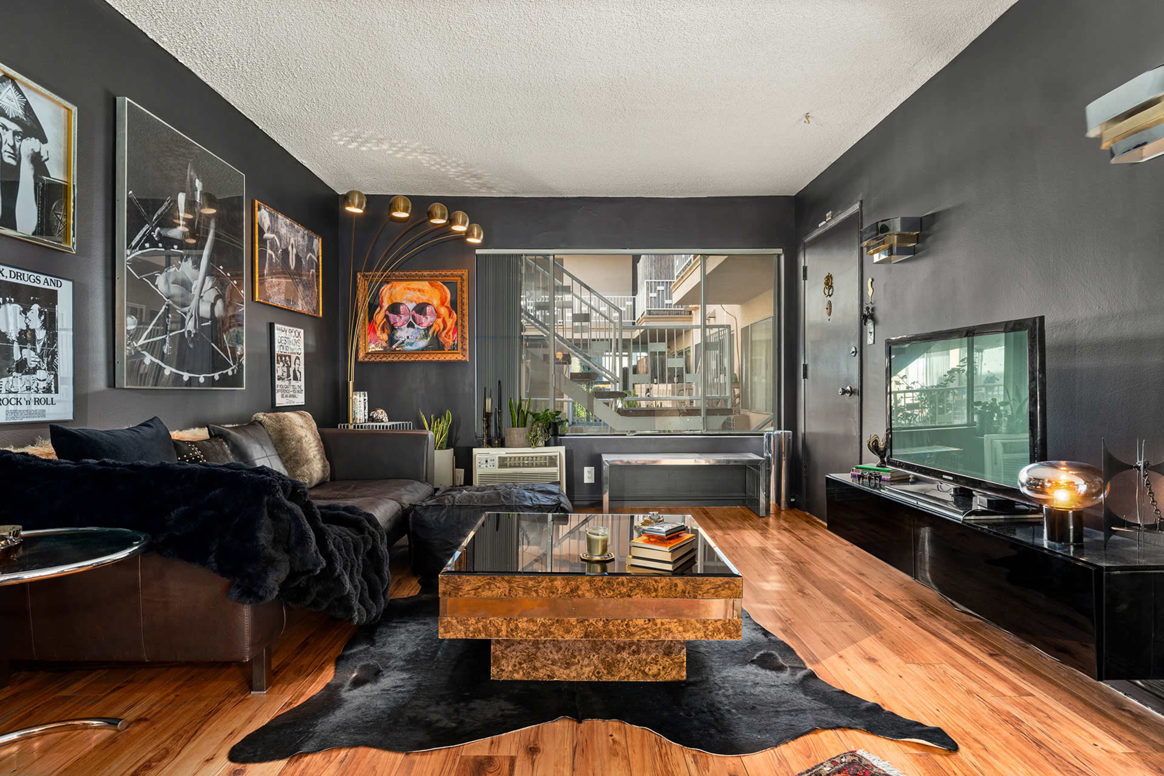 The living room features dark walls, a glass coffee table, a sofa, and several framed artworks.