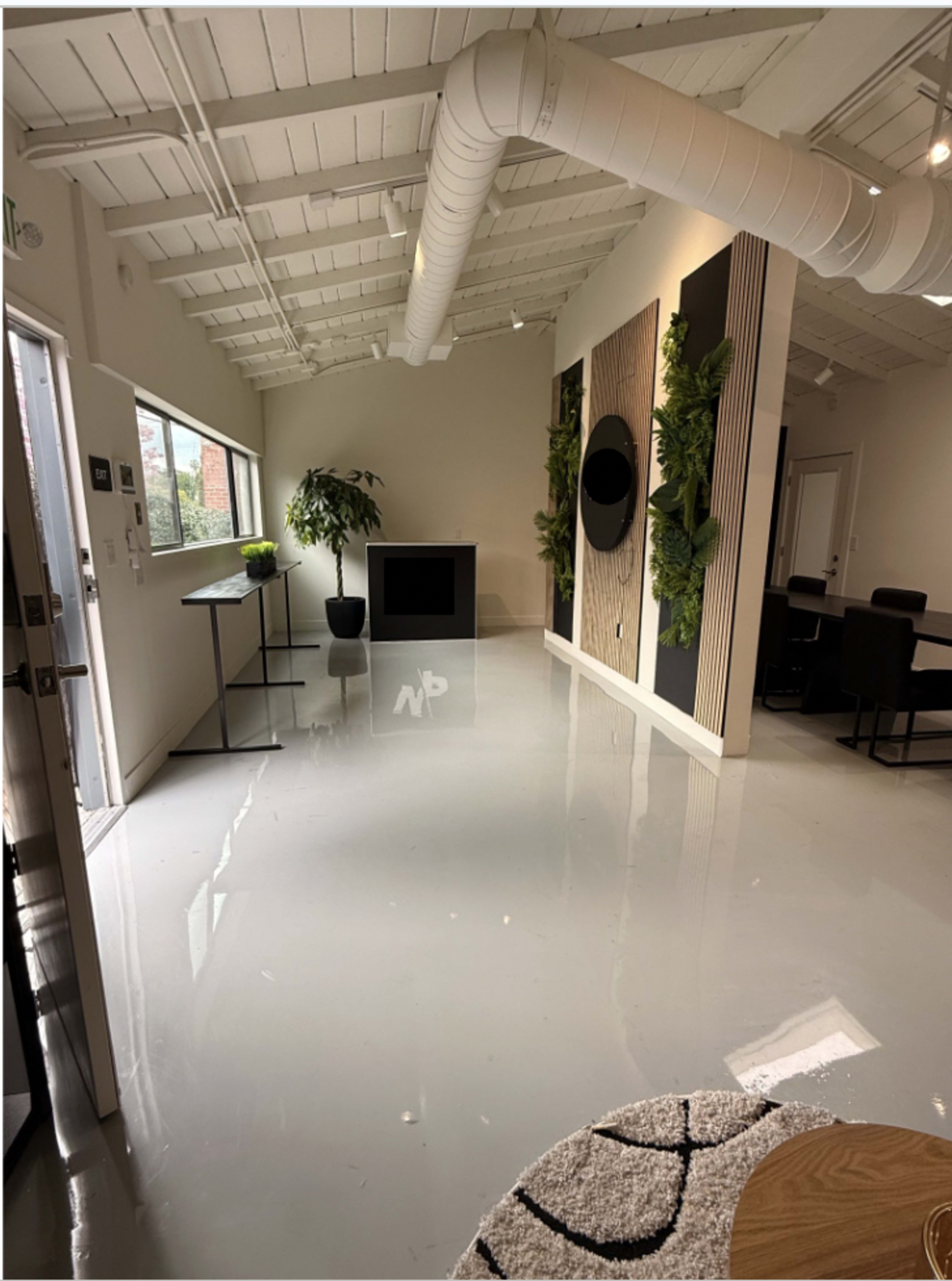 The image shows a modern, open interior space with light-colored walls, a glossy floor, and plants integrated into the decor.
