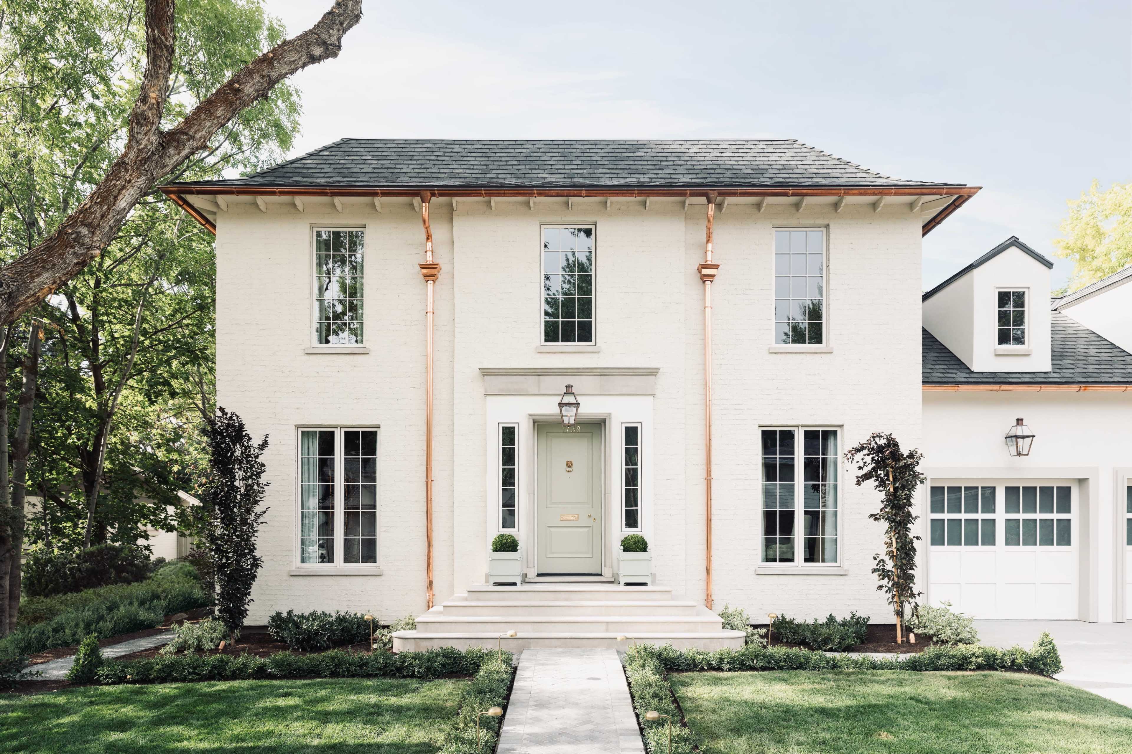 A two-story white brick house with large windows and a stone pathway leading to the front door.