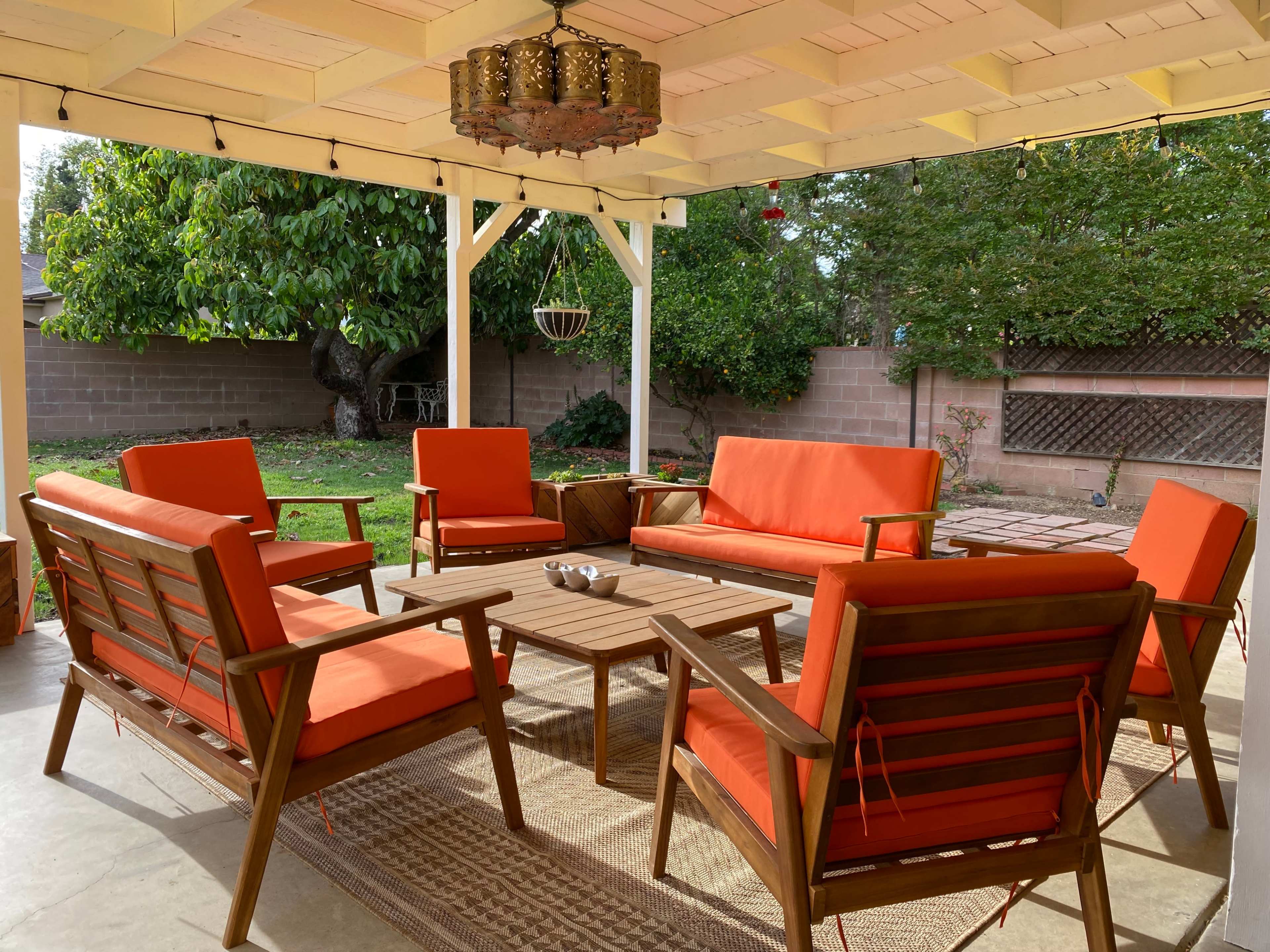 A cozy outdoor seating area features orange cushioned chairs and a coffee table beneath a pergola.