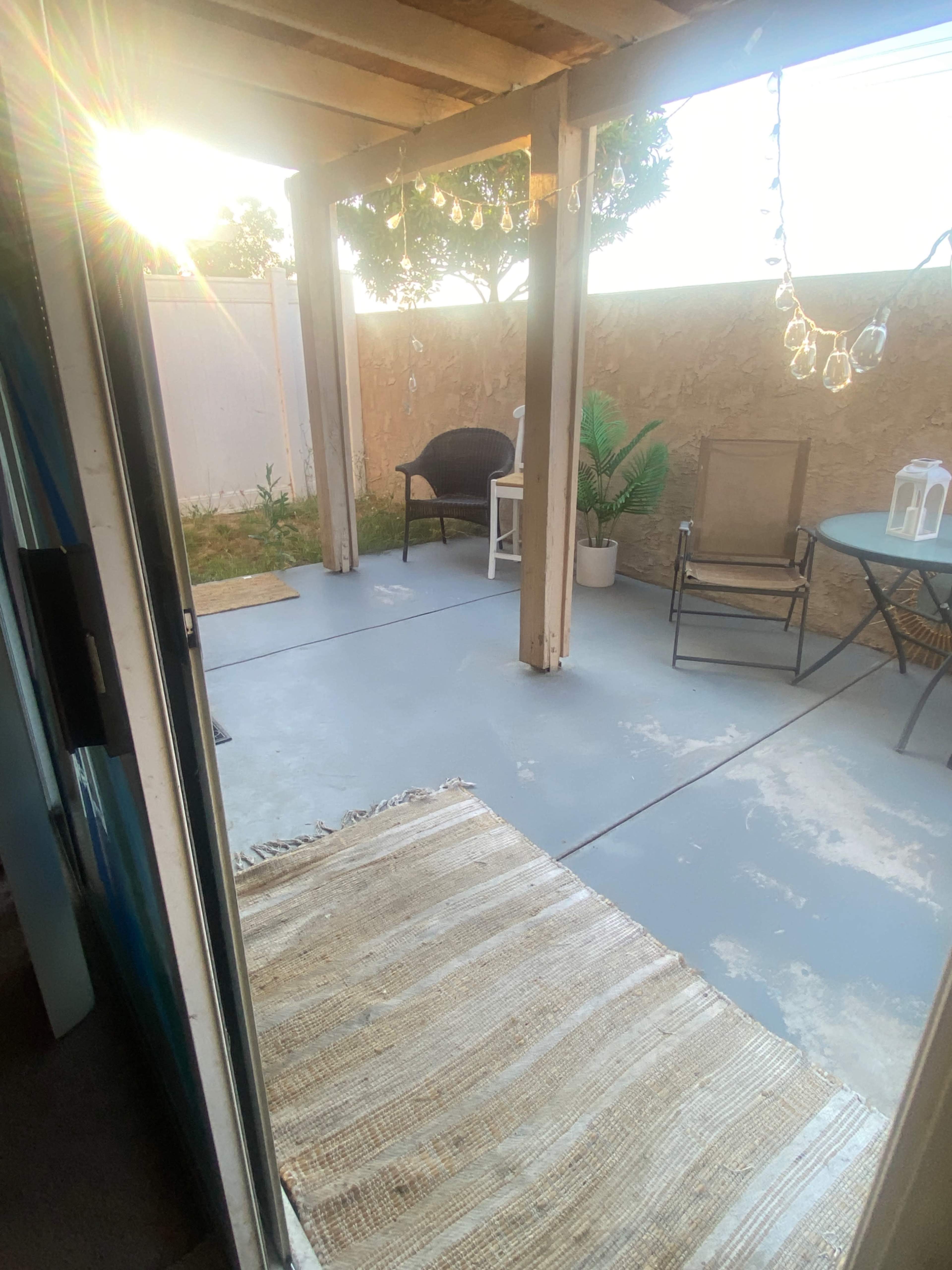The image depicts a partially shaded outdoor patio area with a table, chairs, and a potted plant, illuminated by afternoon sunlight.