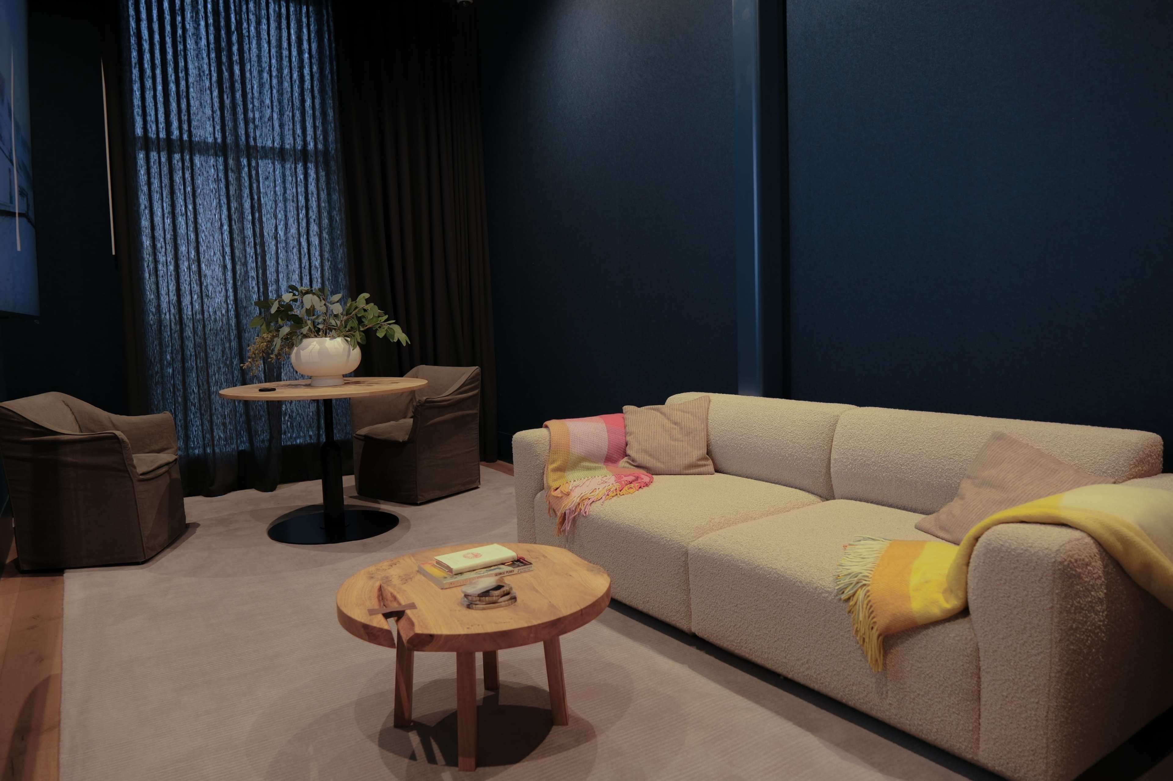A cozy living room featuring a light-colored sofa with colorful throws, a wooden coffee table, and two chairs next to a small round dining table.