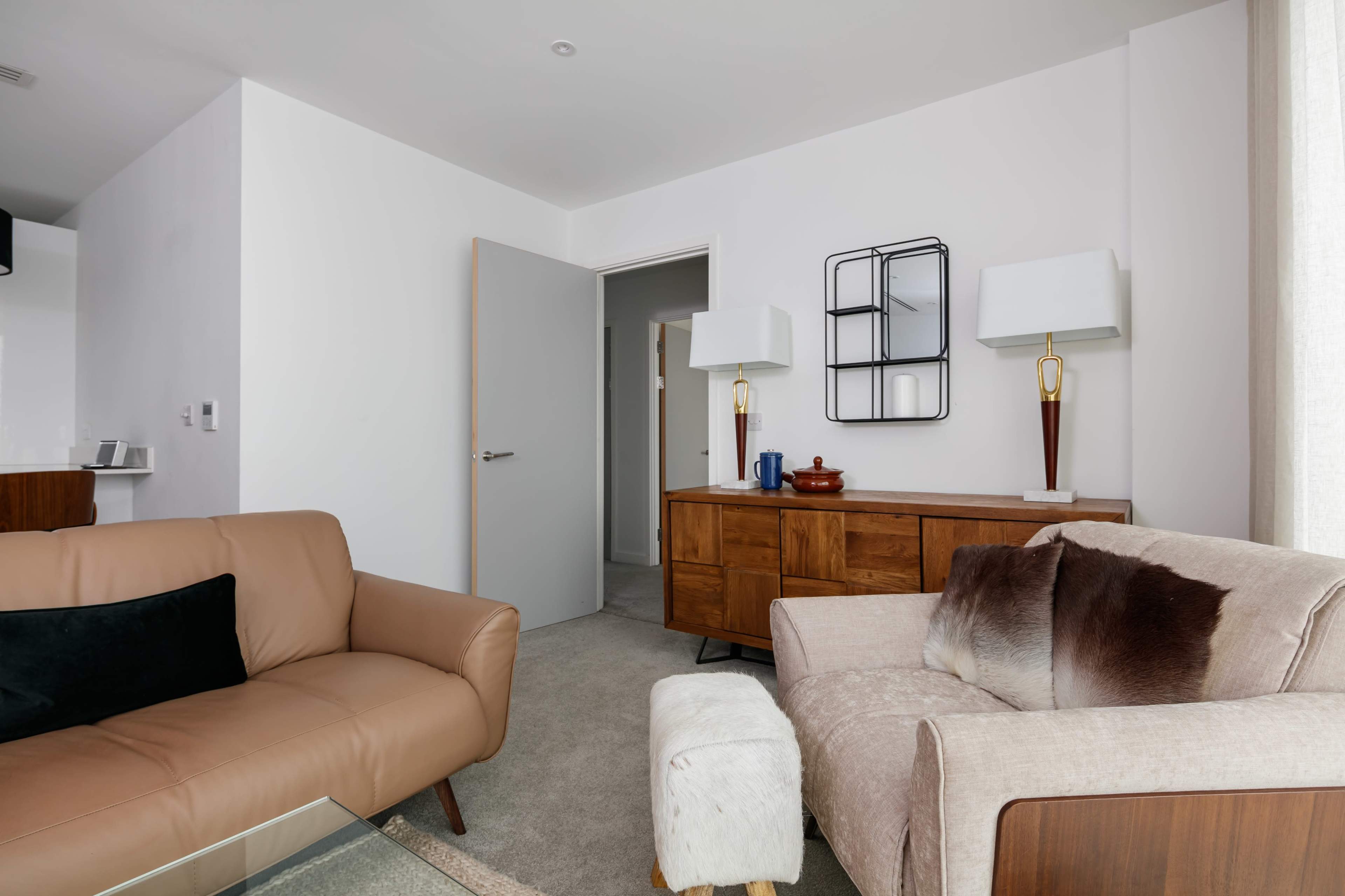 A modern living room with two sofas, a wooden sideboard, and lamps on either side of a decorative mirror.