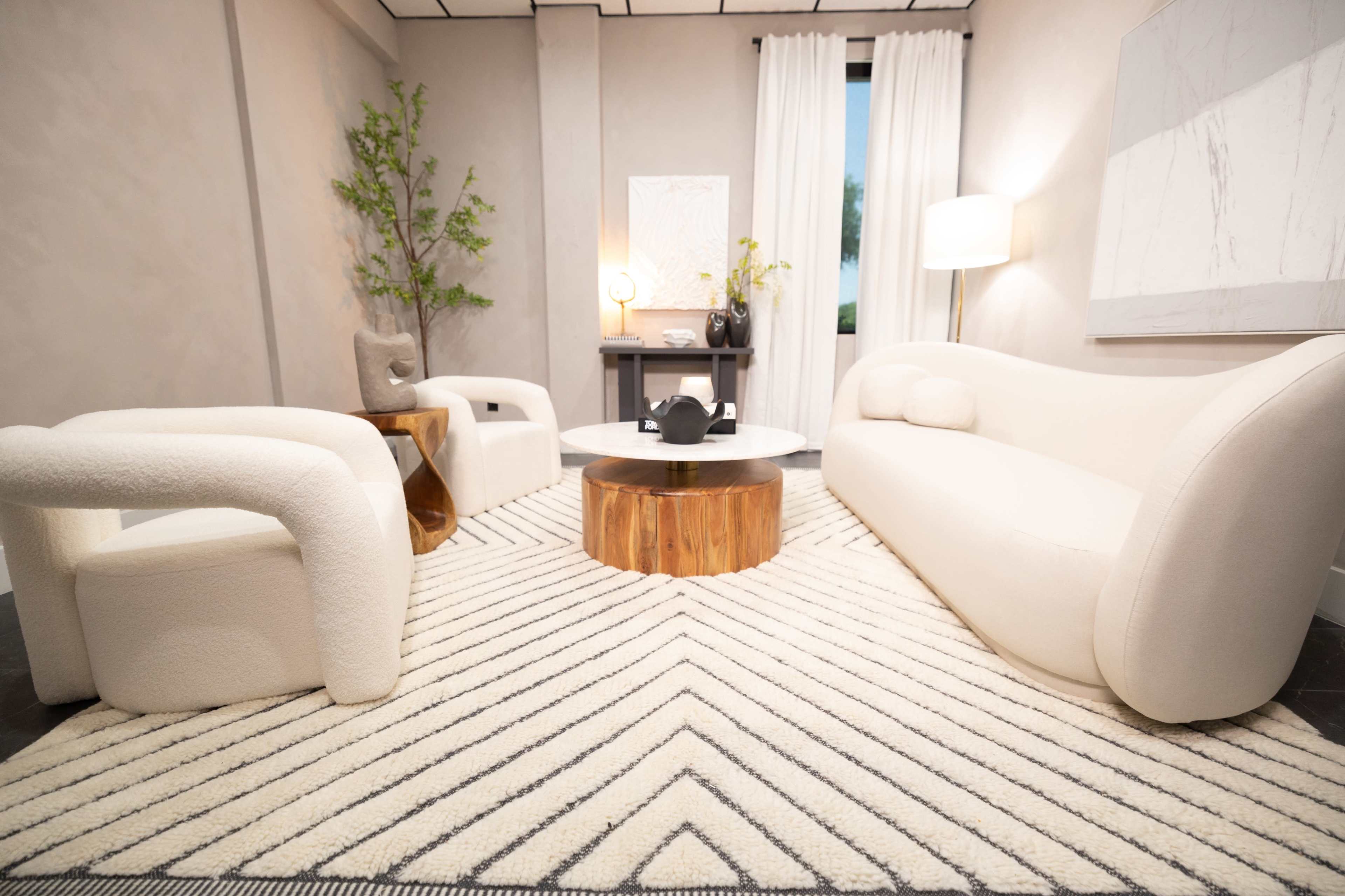 A modern living room with two white sofas, a round wooden coffee table, and a patterned area rug.