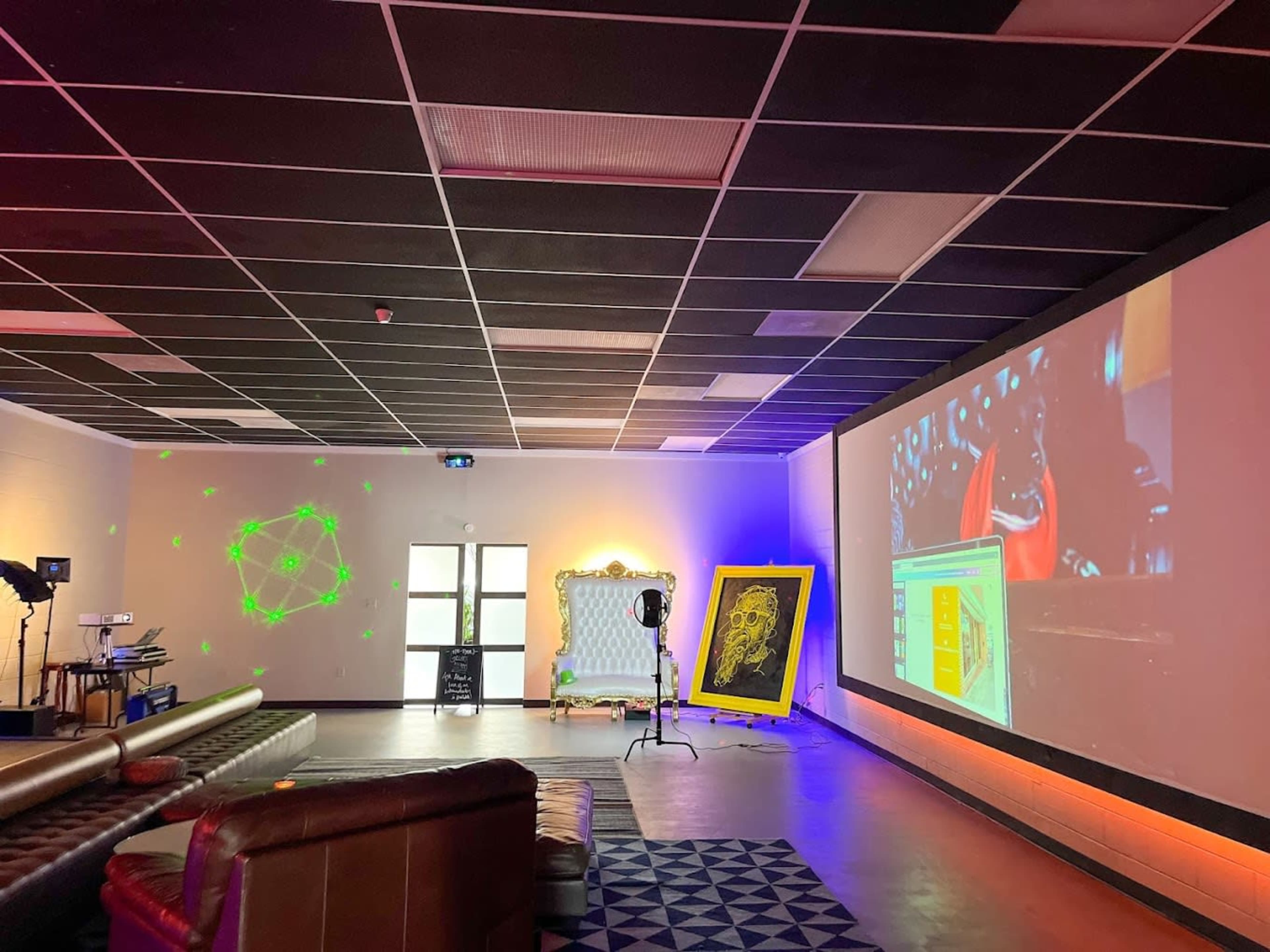 A spacious room with a large screen displaying a presentation, a decorative frame on the floor, and a seating area featuring a sofa.