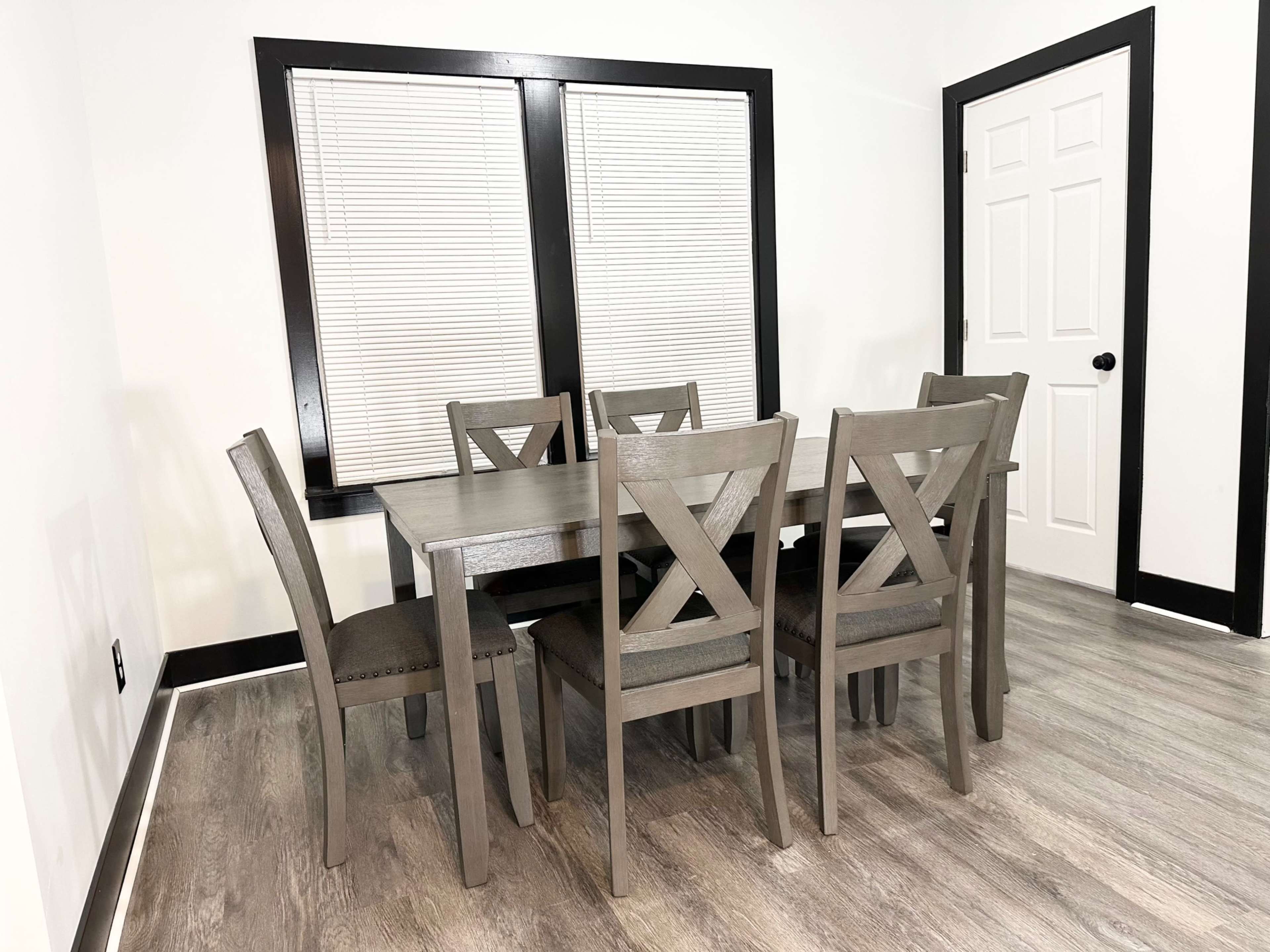 A wooden dining table with eight chairs is positioned in a room featuring white walls and black trim.