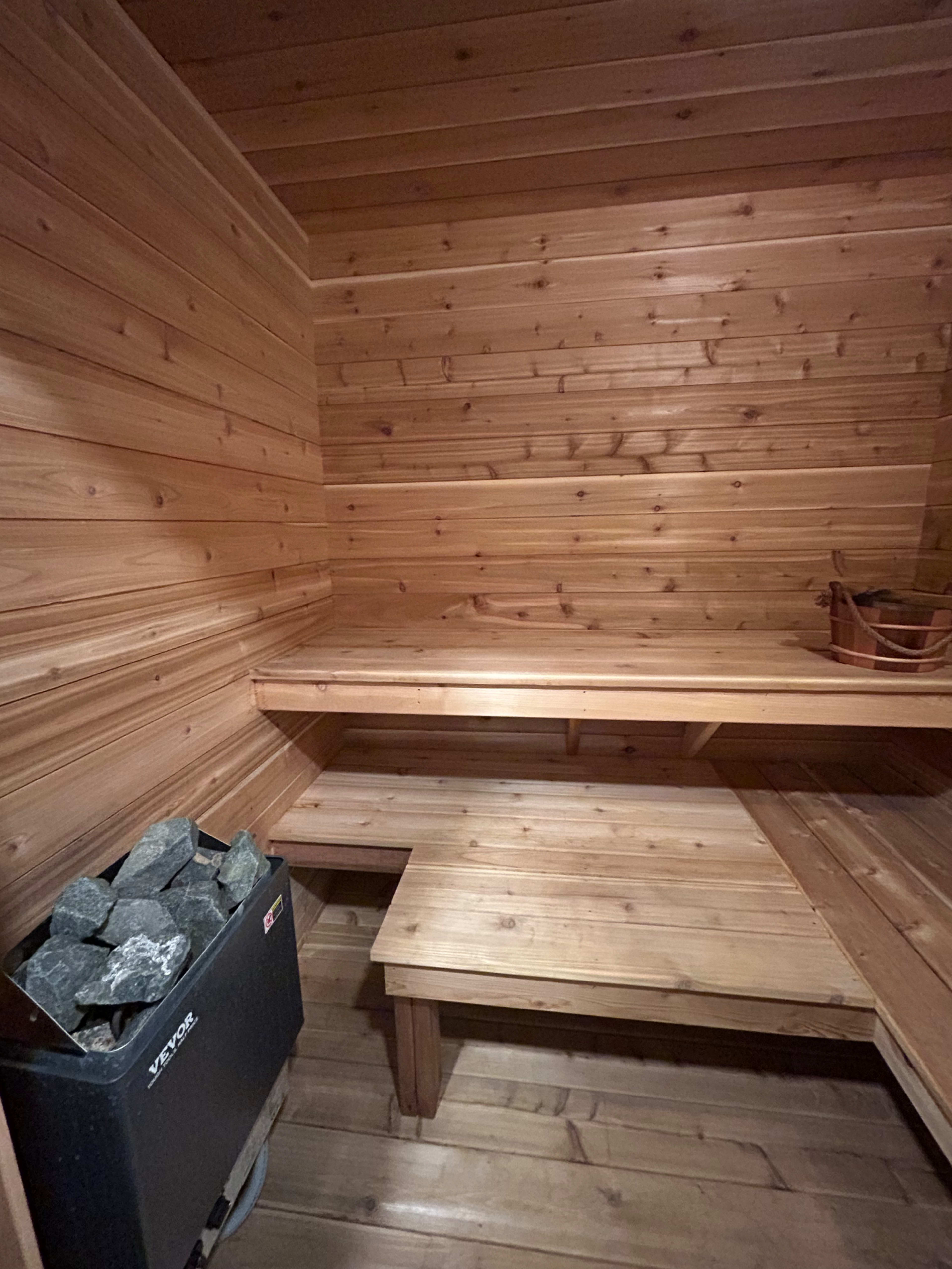 The image shows a wooden sauna interior with benches and a stone heater in one corner.