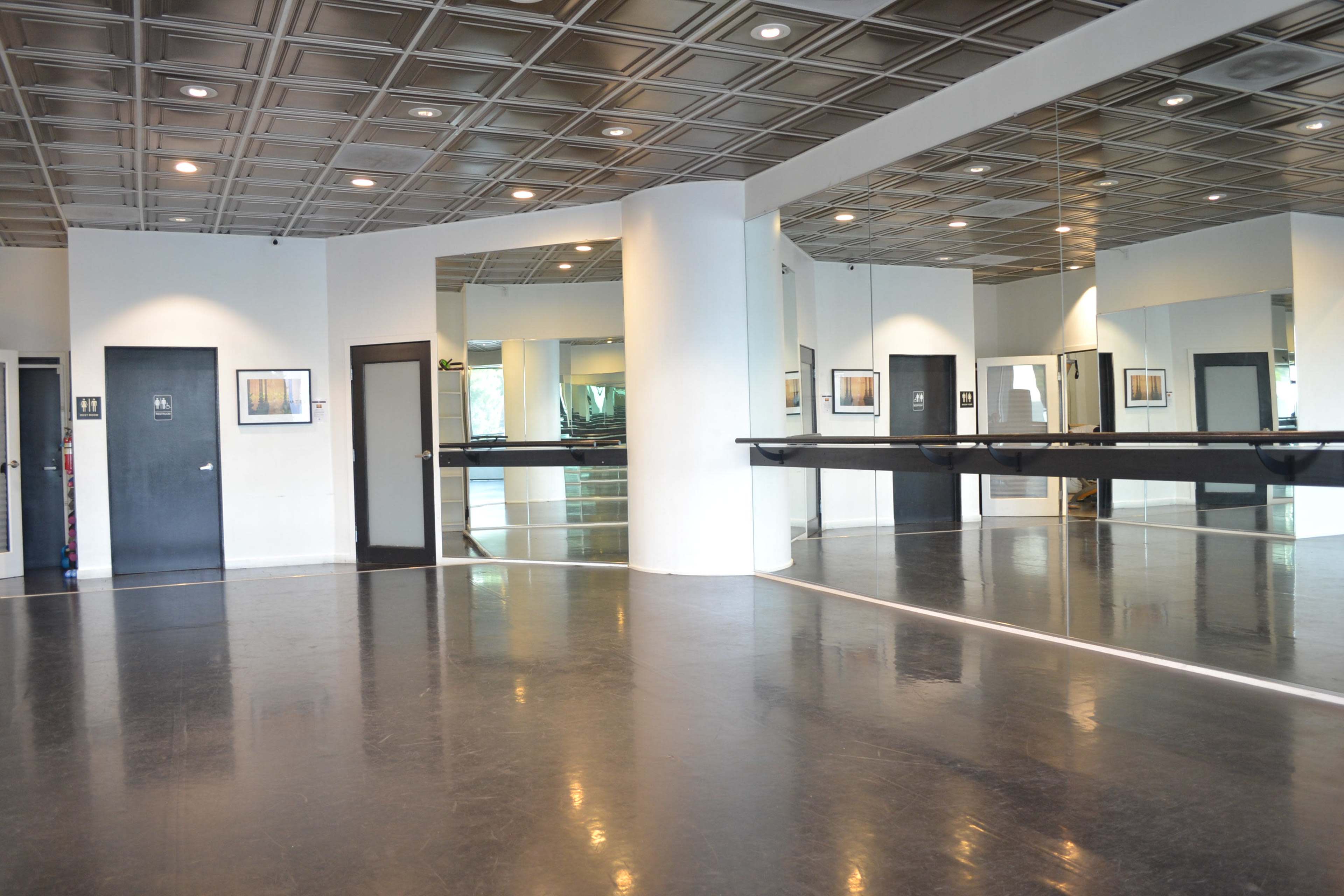 A spacious dance studio with a mirrored wall, polished black floor, and a ceiling with decorative tiles.
