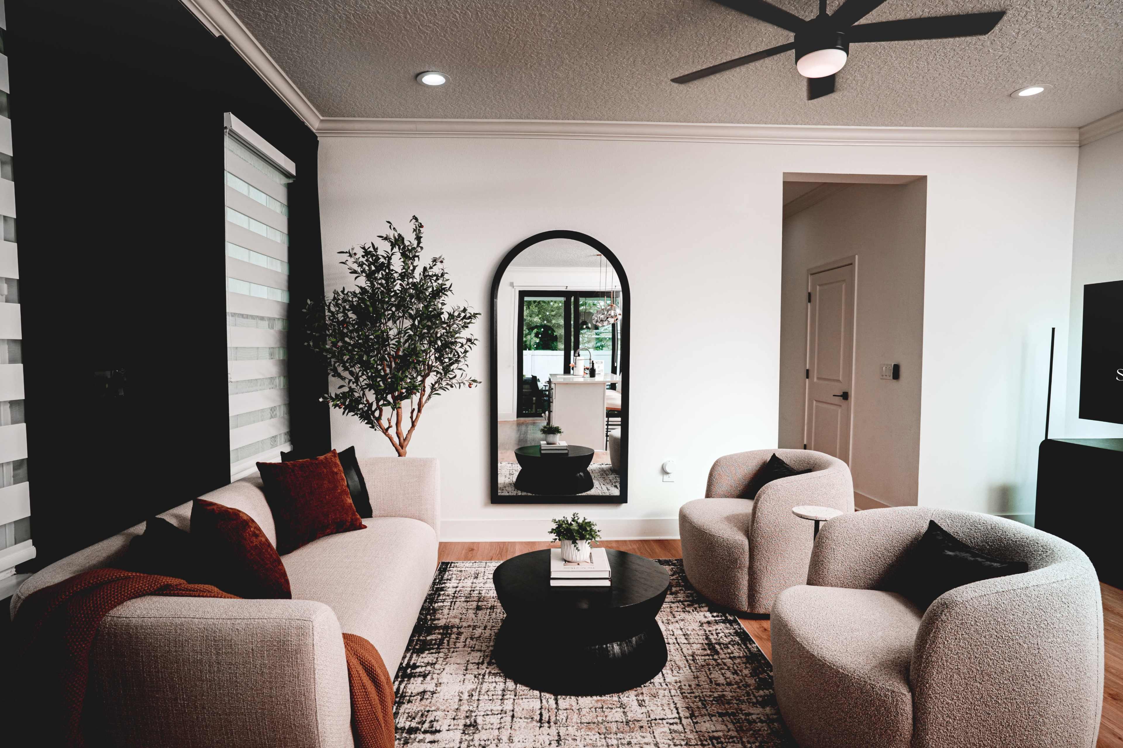 A modern living room features a sofa, two armchairs, a round coffee table, and a large mirror reflecting a light and airy space.