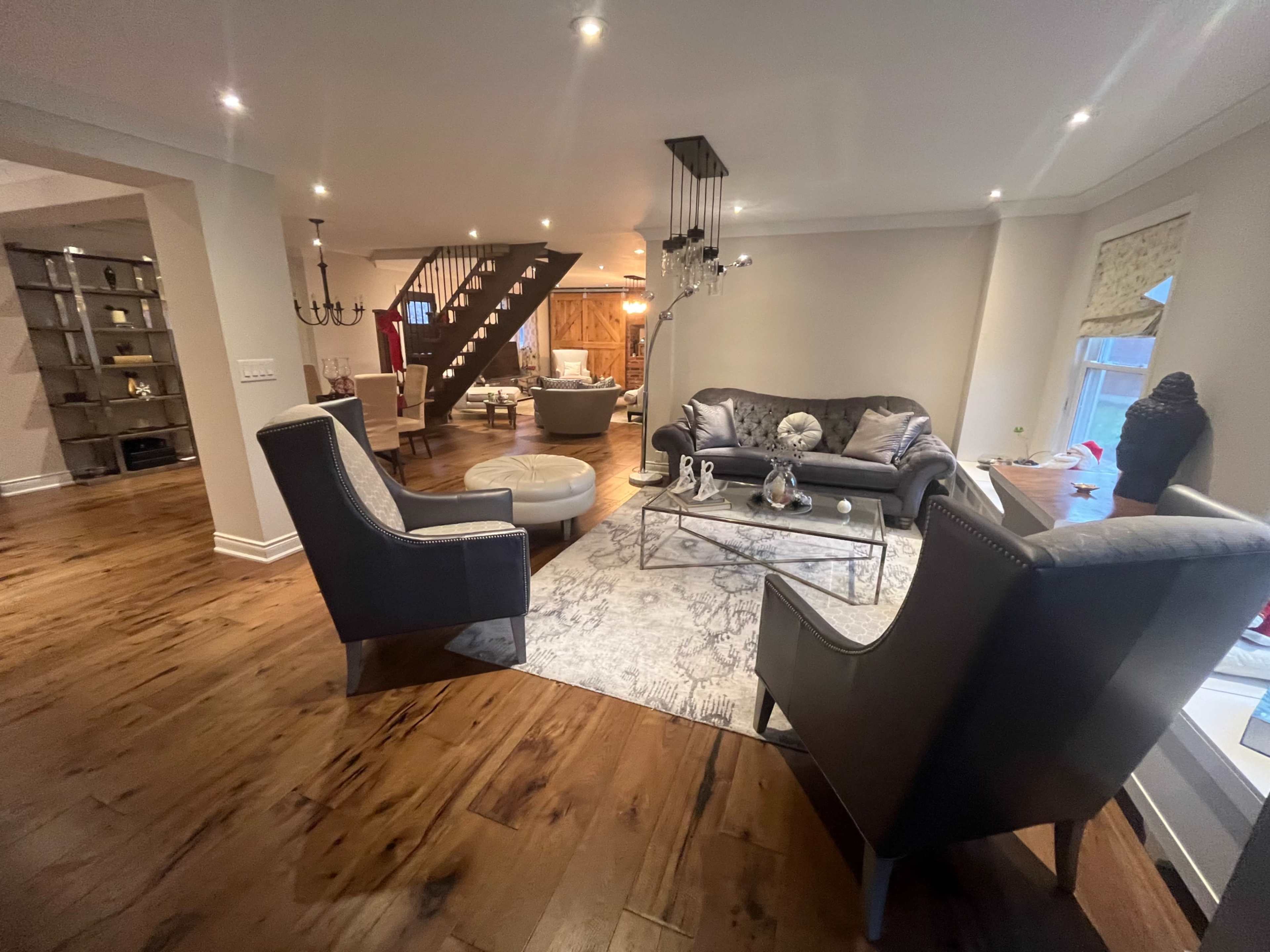 The image shows a modern living room with two armchairs facing a sofa, a coffee table in the center, and a staircase visible in the background.