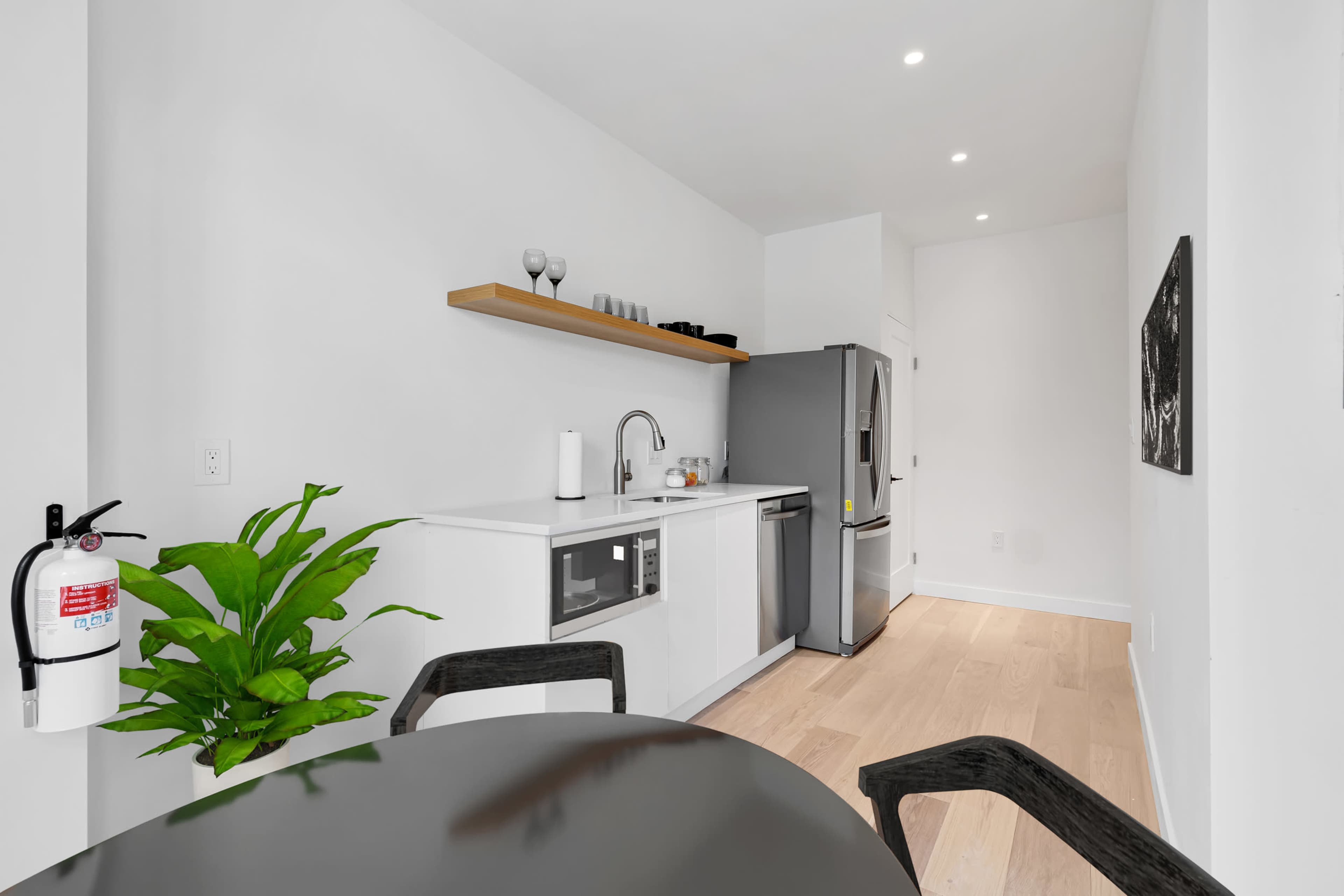 A modern kitchen features a stainless steel refrigerator, a sink area, and a plant beside a round dining table.