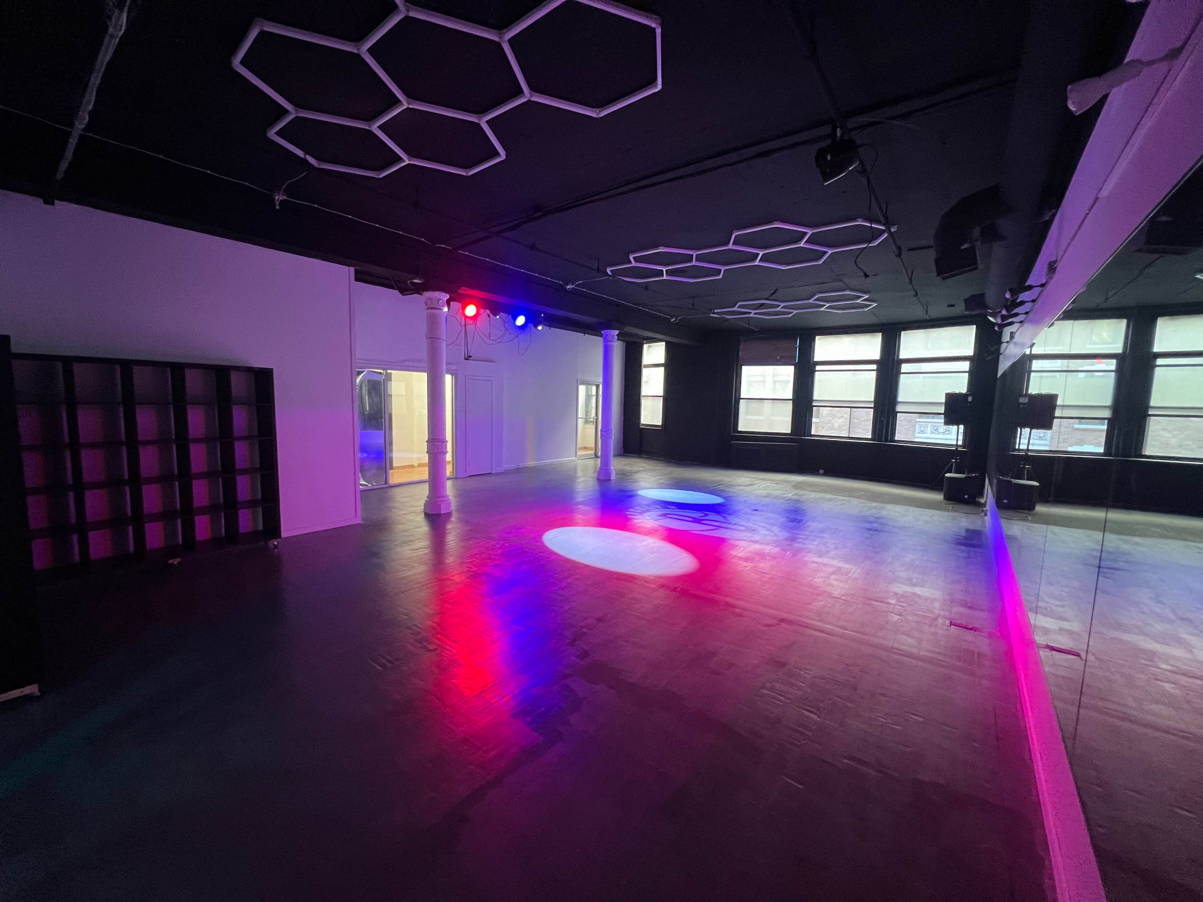 The image shows a spacious, empty room with honeycomb-patterned light fixtures on the ceiling and colored lights illuminating the floor.