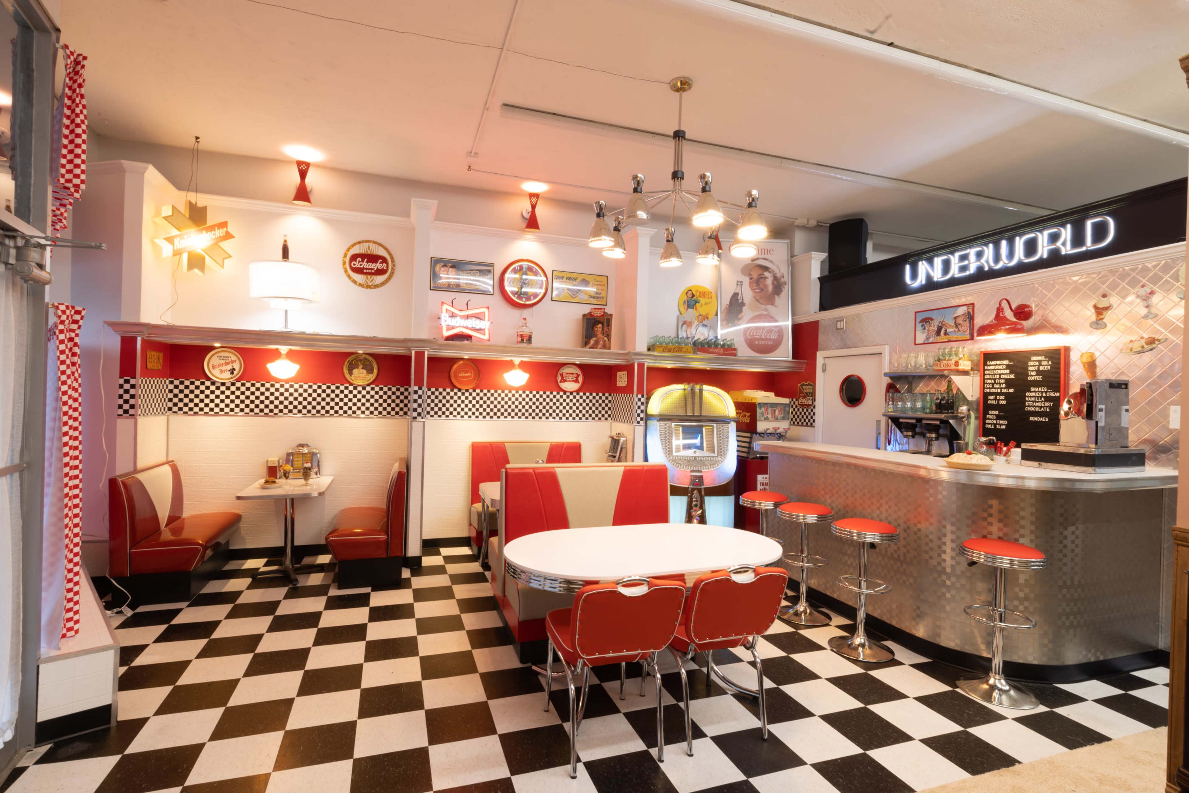 A retro-style diner featuring red and white furnishings, checkered flooring, and a jukebox near the counter.