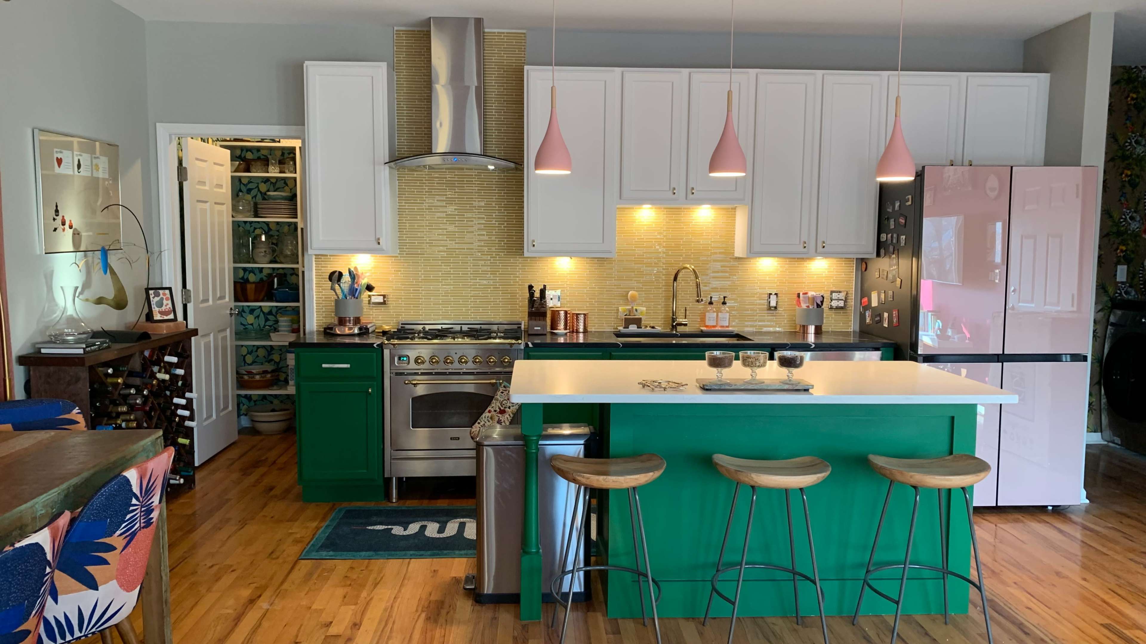 The kitchen features green cabinets, a white island with bar stools, and modern appliances, complemented by a mosaic backsplash and pendant lights.