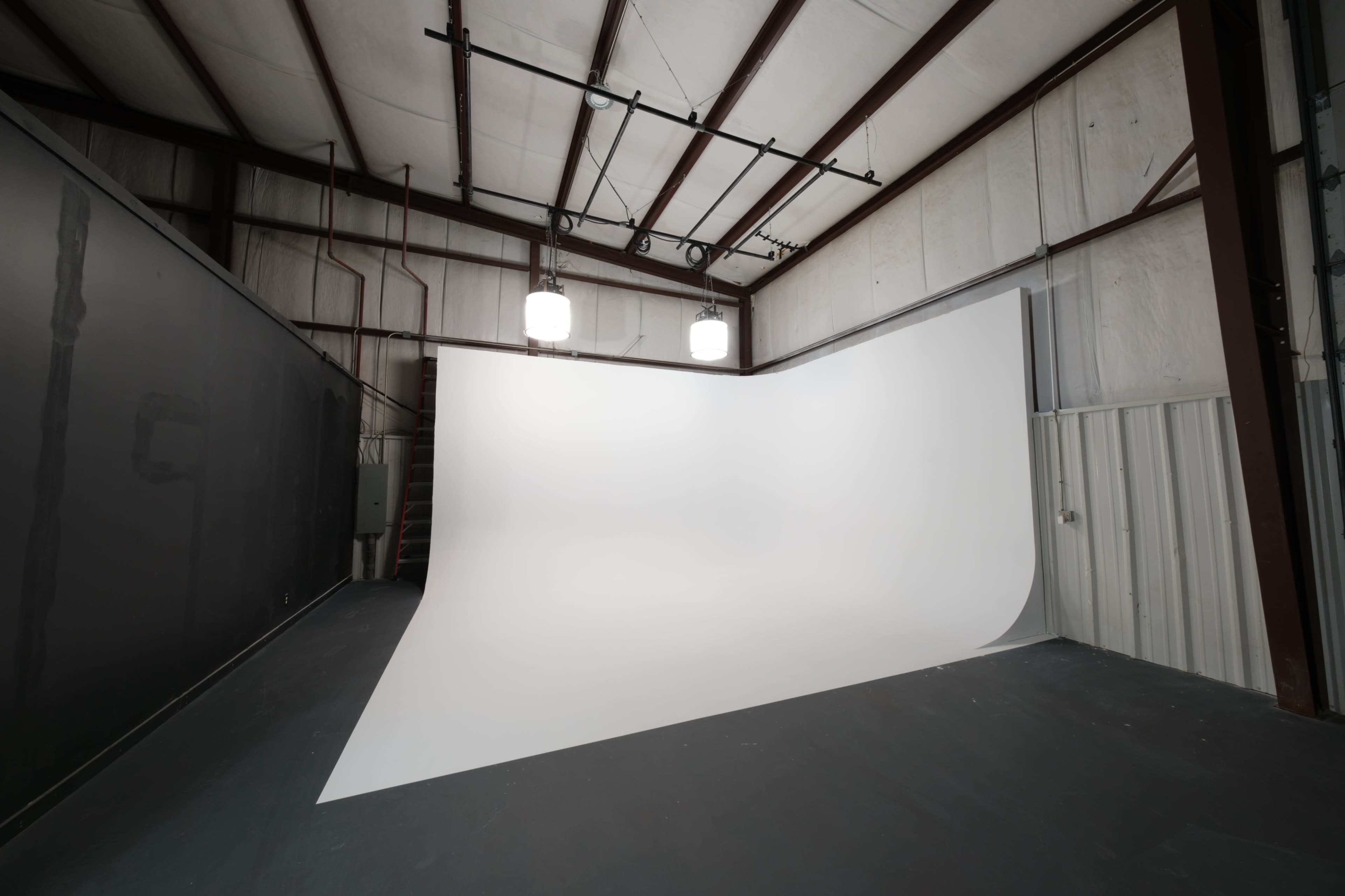 The image shows a spacious photography studio with a large, curved white backdrop and overhead lighting.