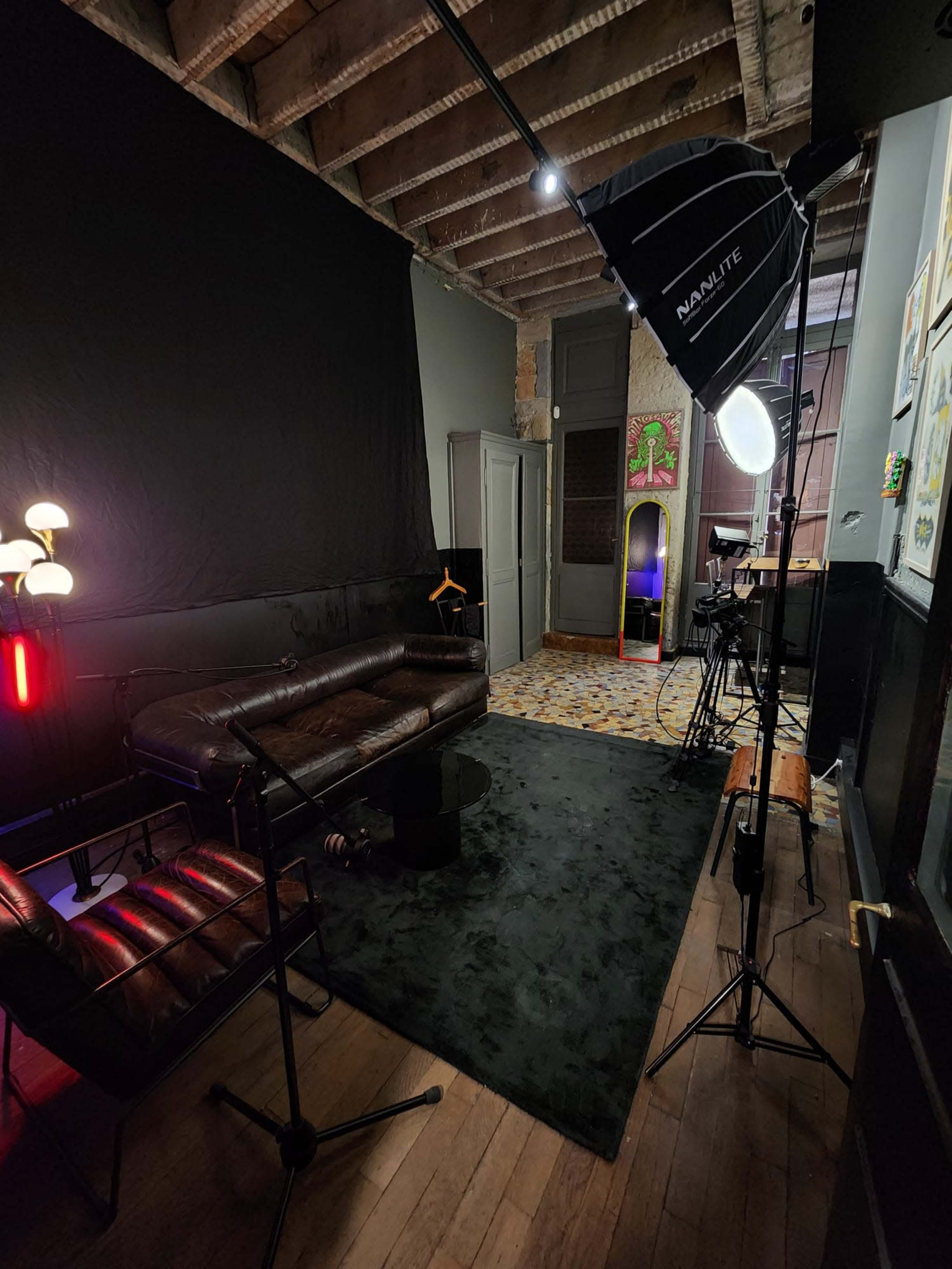 A room set up for a video or photo shoot, featuring a black backdrop, a leather sofa, a coffee table, and lighting equipment.