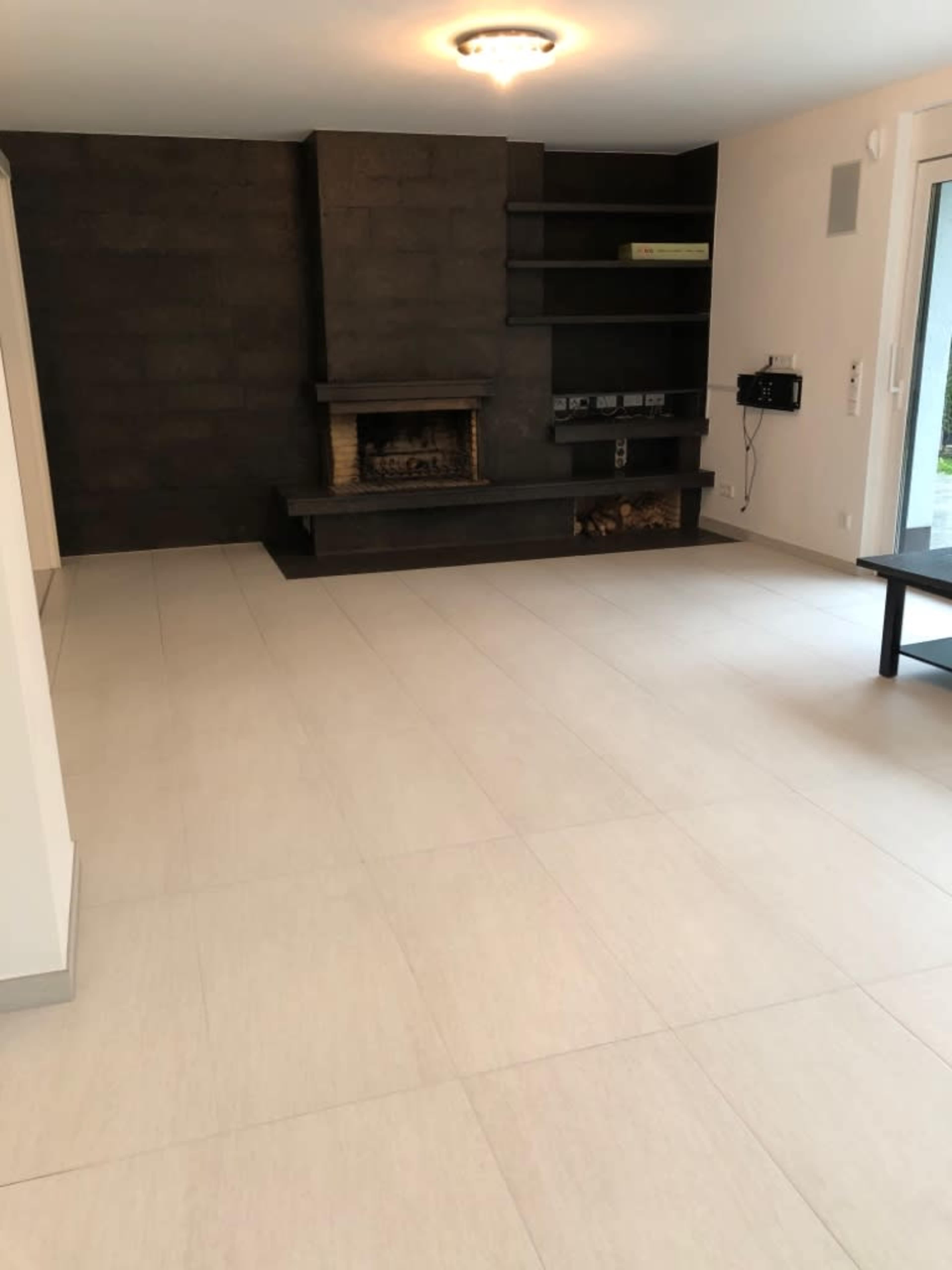 The image shows a modern room with a fireplace, a dark accent wall, and light-colored tile flooring.