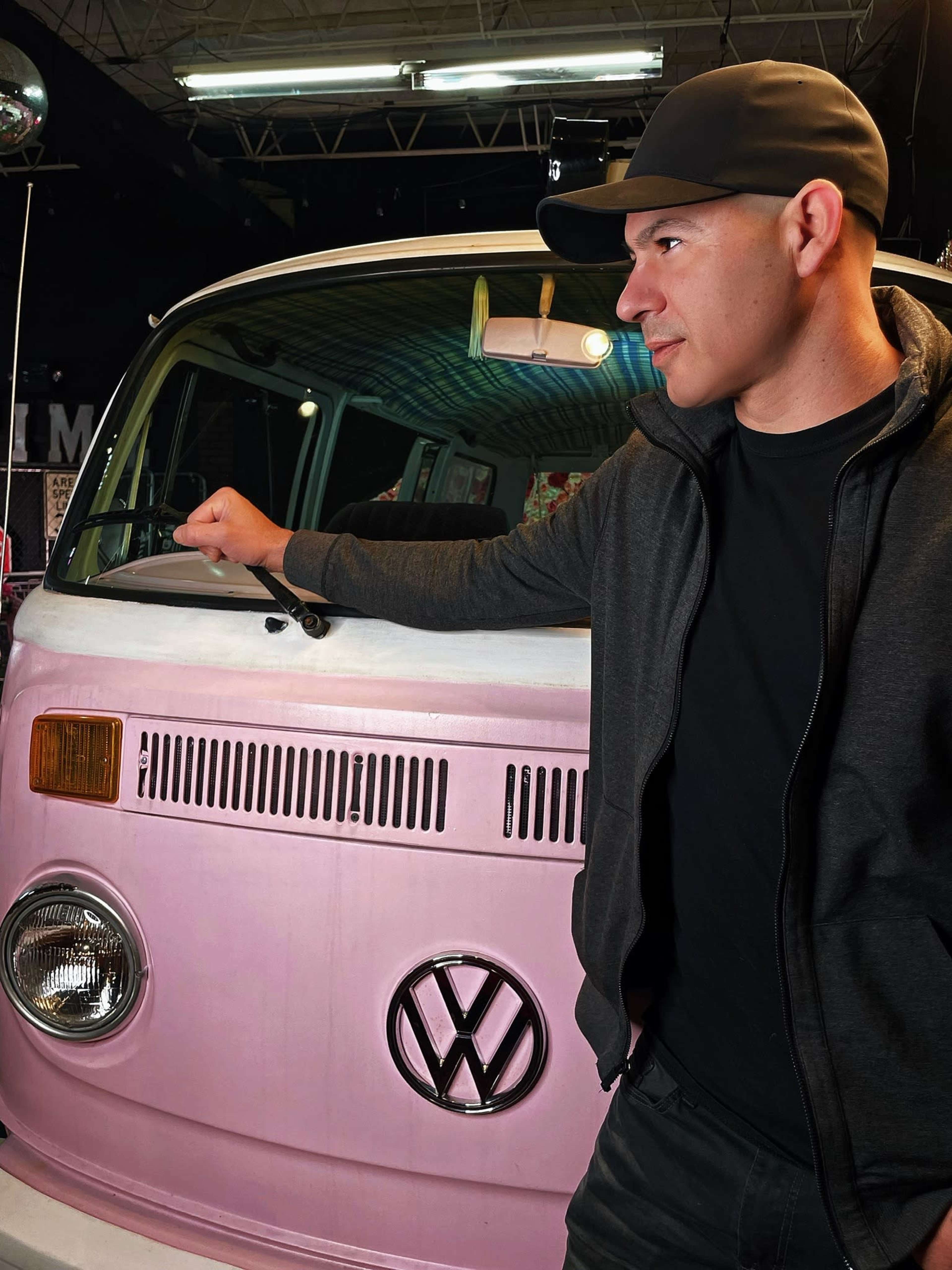A man stands beside a pink Volkswagen van in an indoor setting.