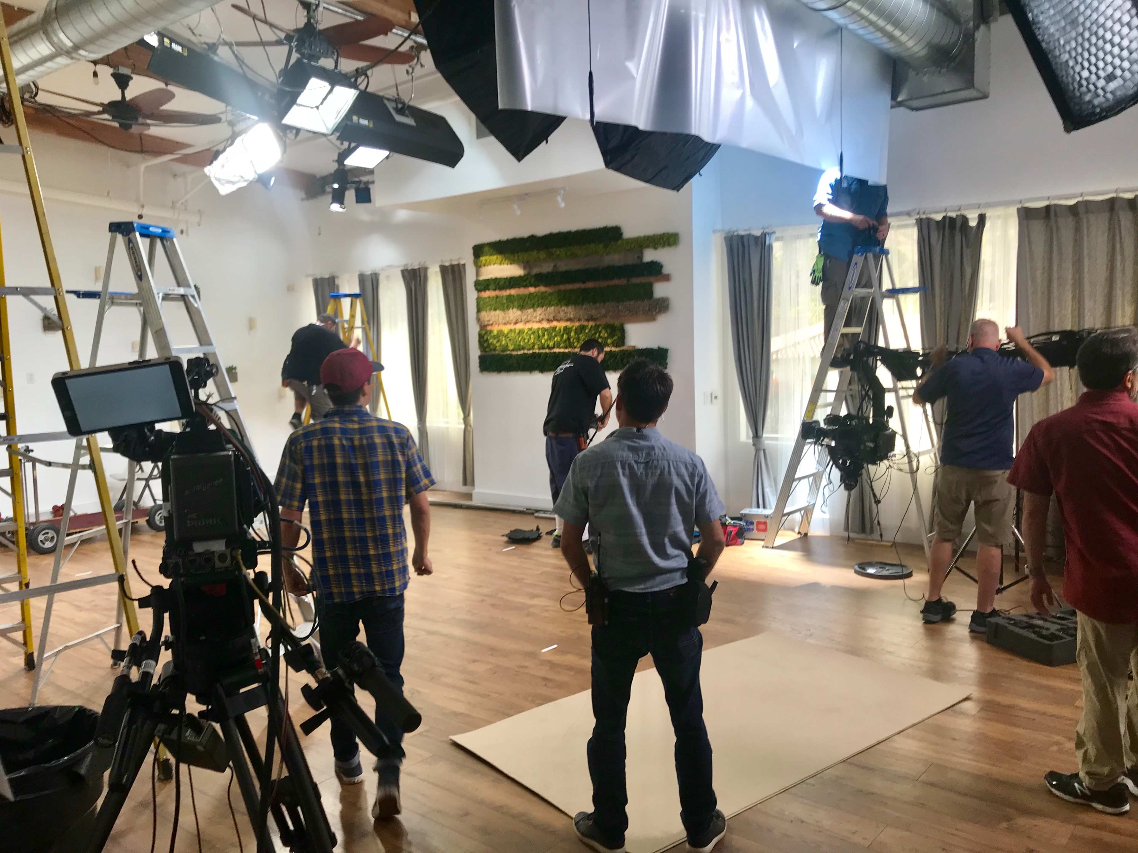 A film crew sets up equipment and lighting in a spacious interior for a production shoot.