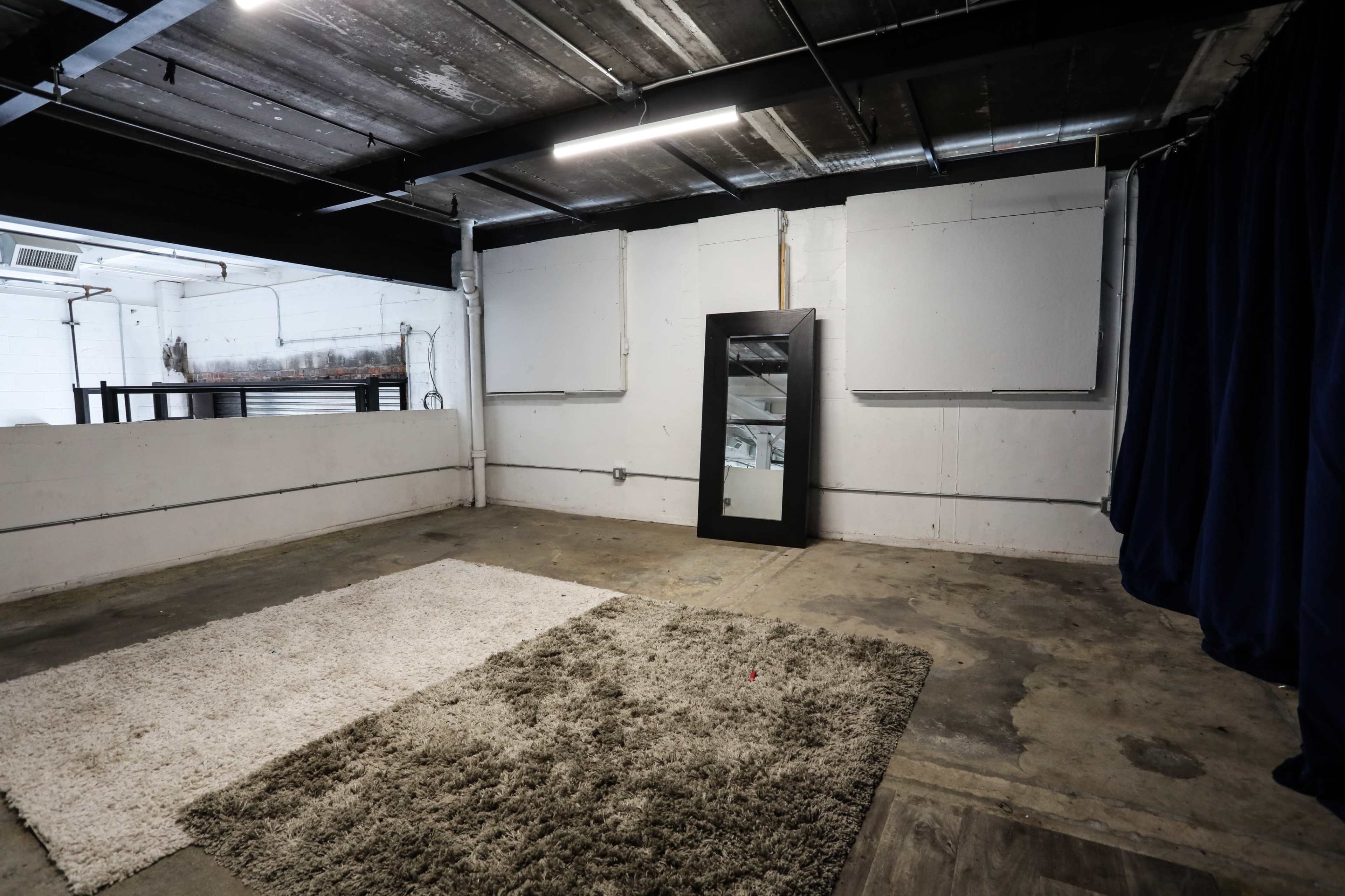 An empty industrial space with a large mirror and a textured rug on the concrete floor.