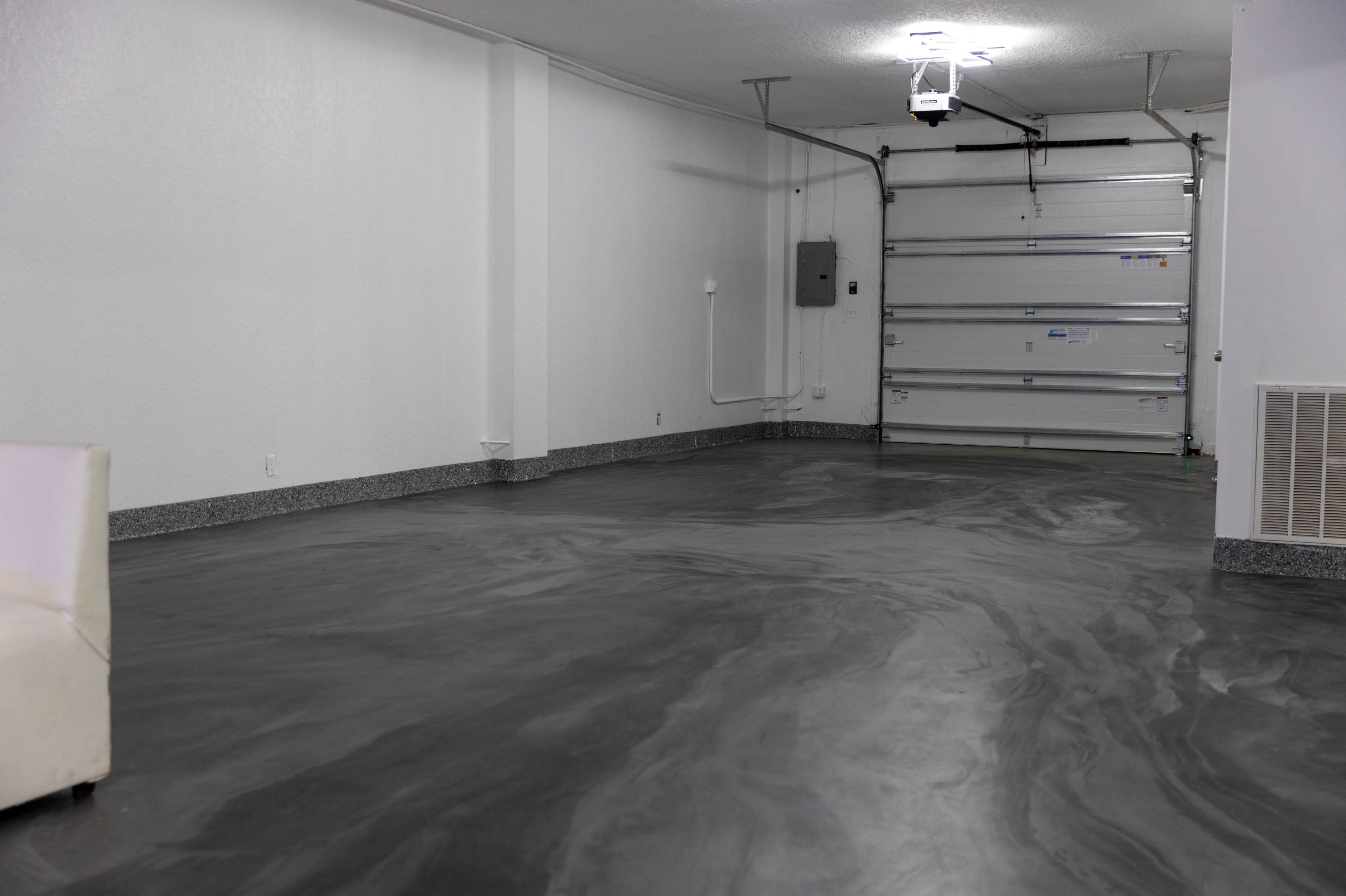 An empty garage with a polished concrete floor and a white wall, featuring a small couch in one corner.