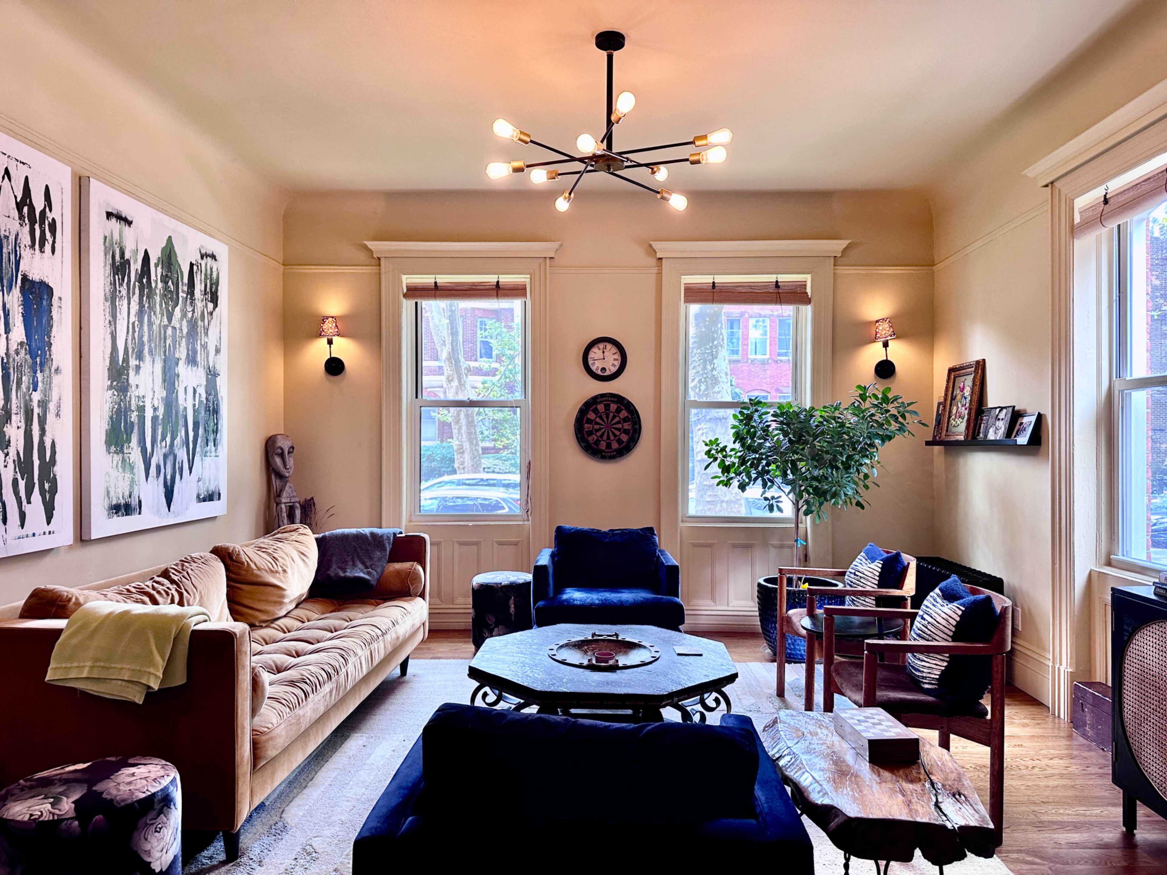 A living room featuring a mix of seating arrangements, art on the walls, and large windows allowing natural light to enter.