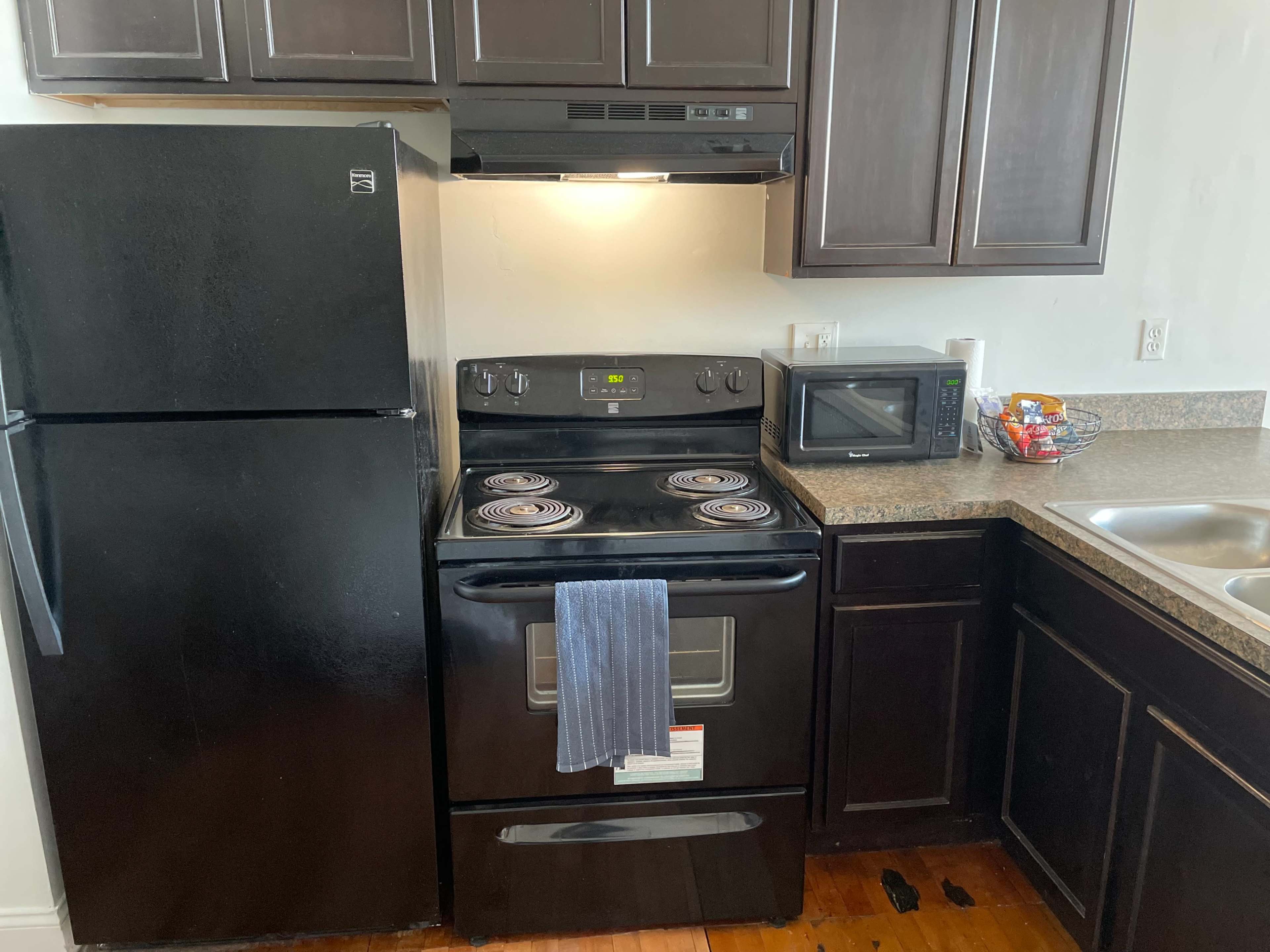 The image shows a kitchen with black appliances, including a refrigerator, stove, and microwave, along with dark wood cabinets and a granite countertop.
