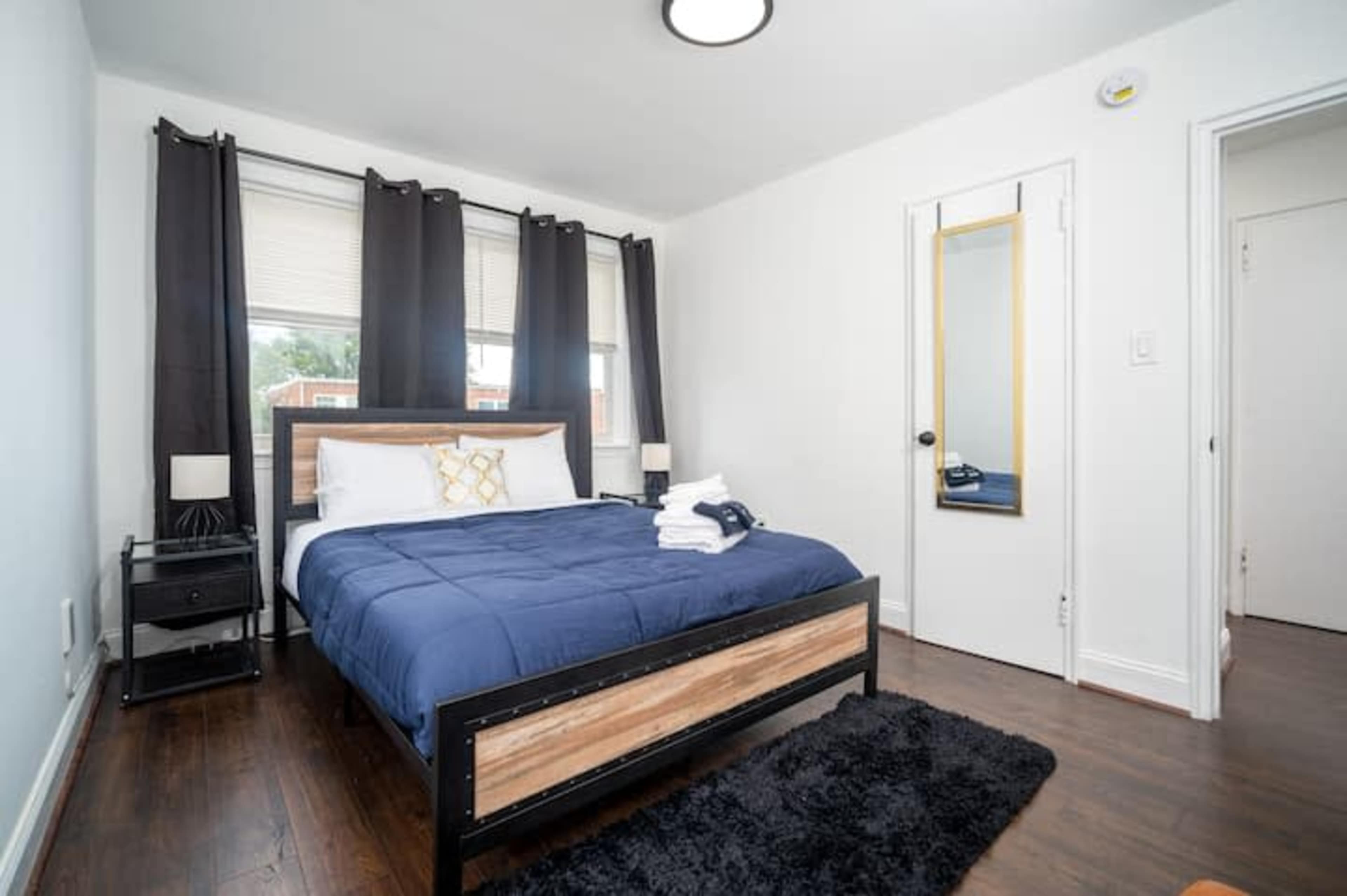 A neatly arranged bedroom featuring a bed with blue bedding, two windows with black curtains, and a mirrored closet.