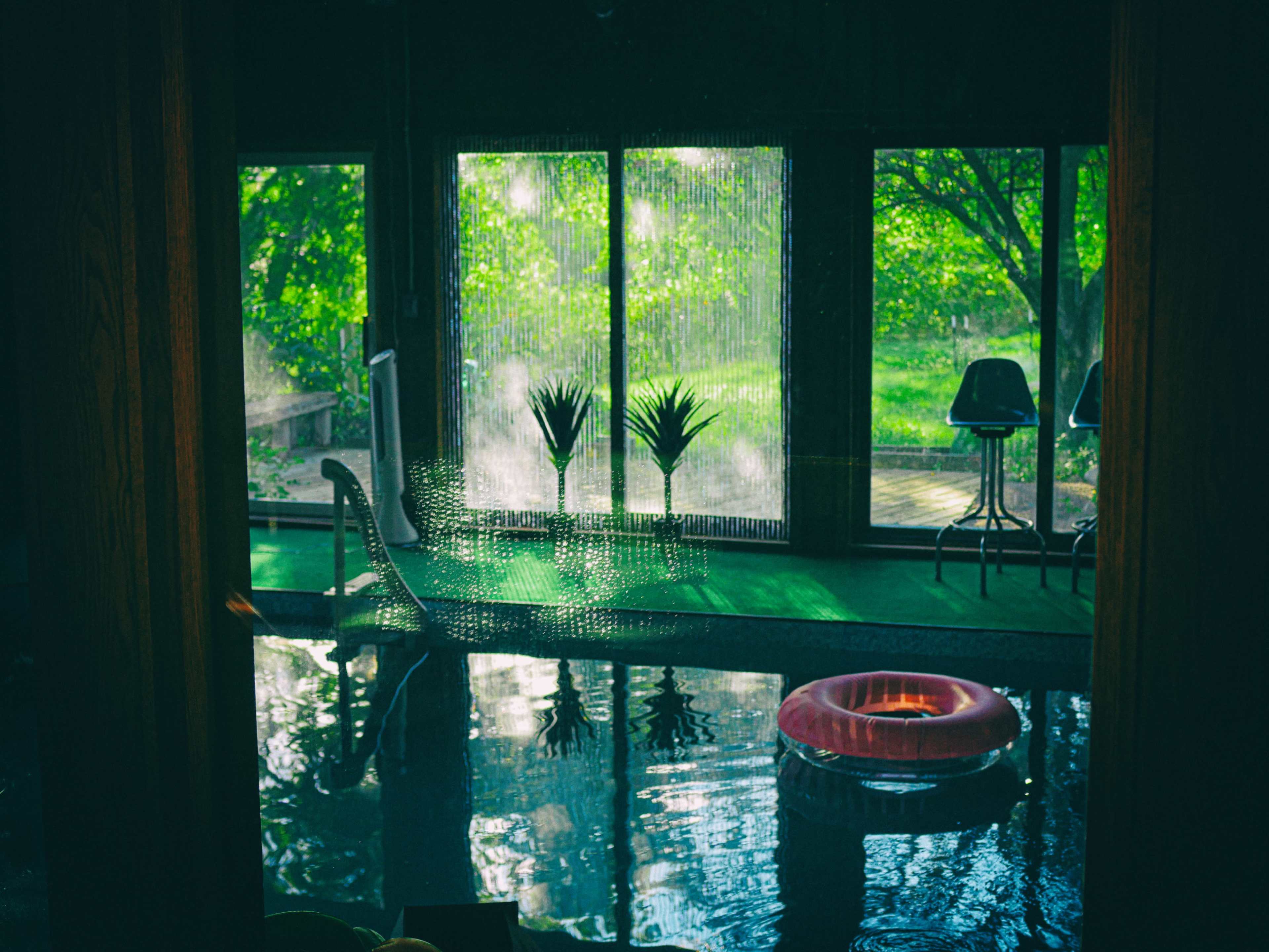 The image shows an indoor pool area with a pink inflatable ring and large windows overlooking a green landscape.