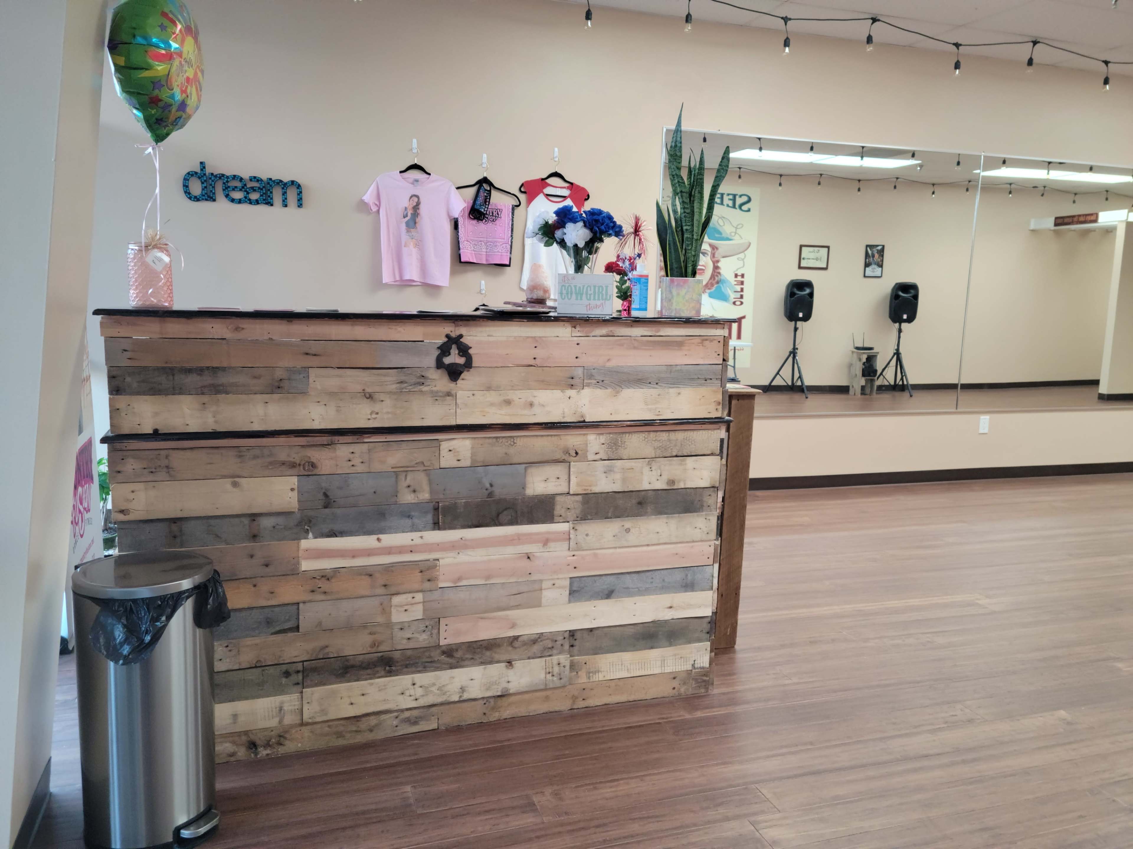 A wooden reception desk made from pallets, with decorations and clothing displayed on the wall behind it in a spacious, well-lit room.