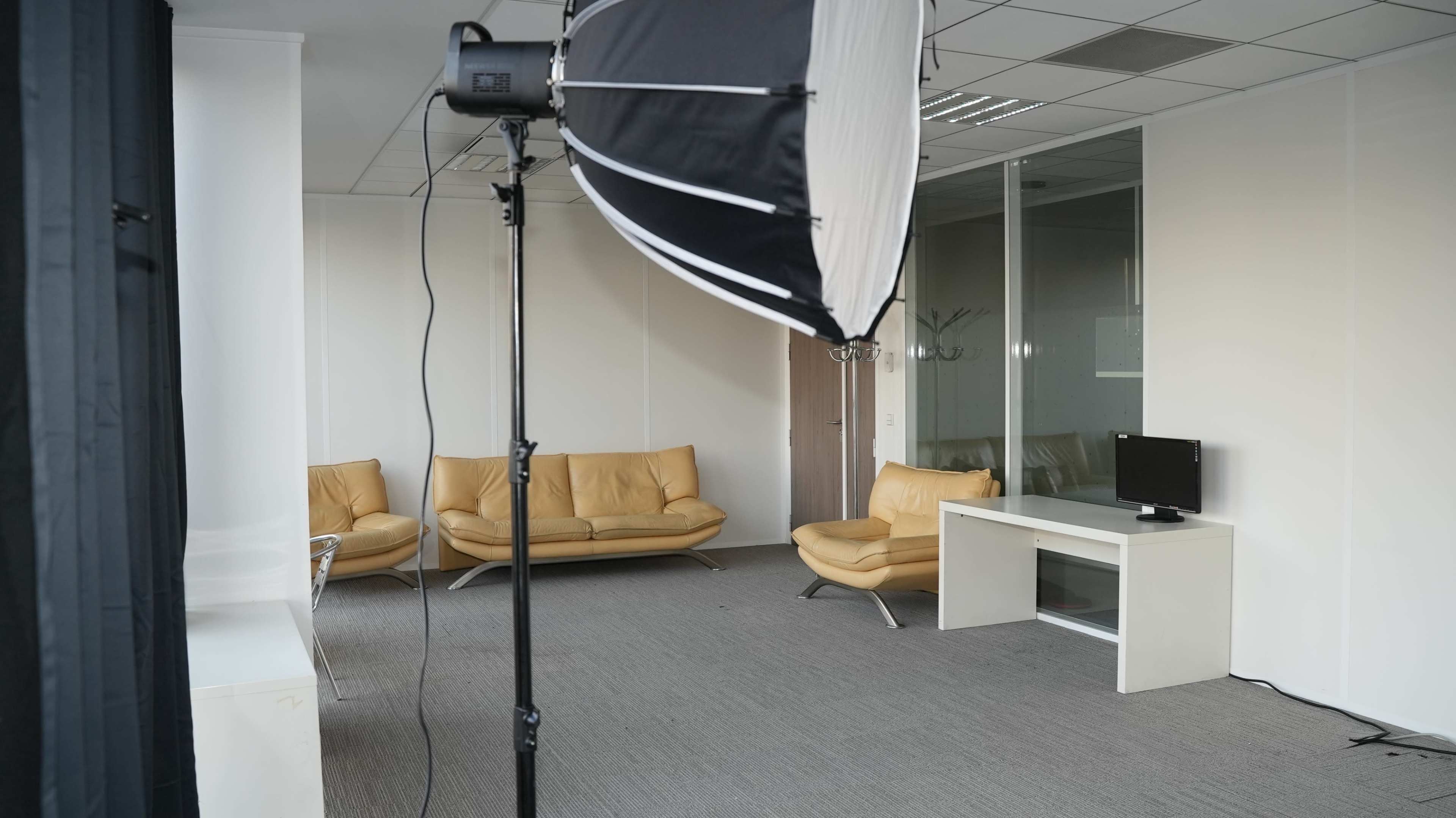 The image shows a minimalist office space with two yellow leather sofas, a white TV stand, and a small television on it, illuminated by a softbox light.