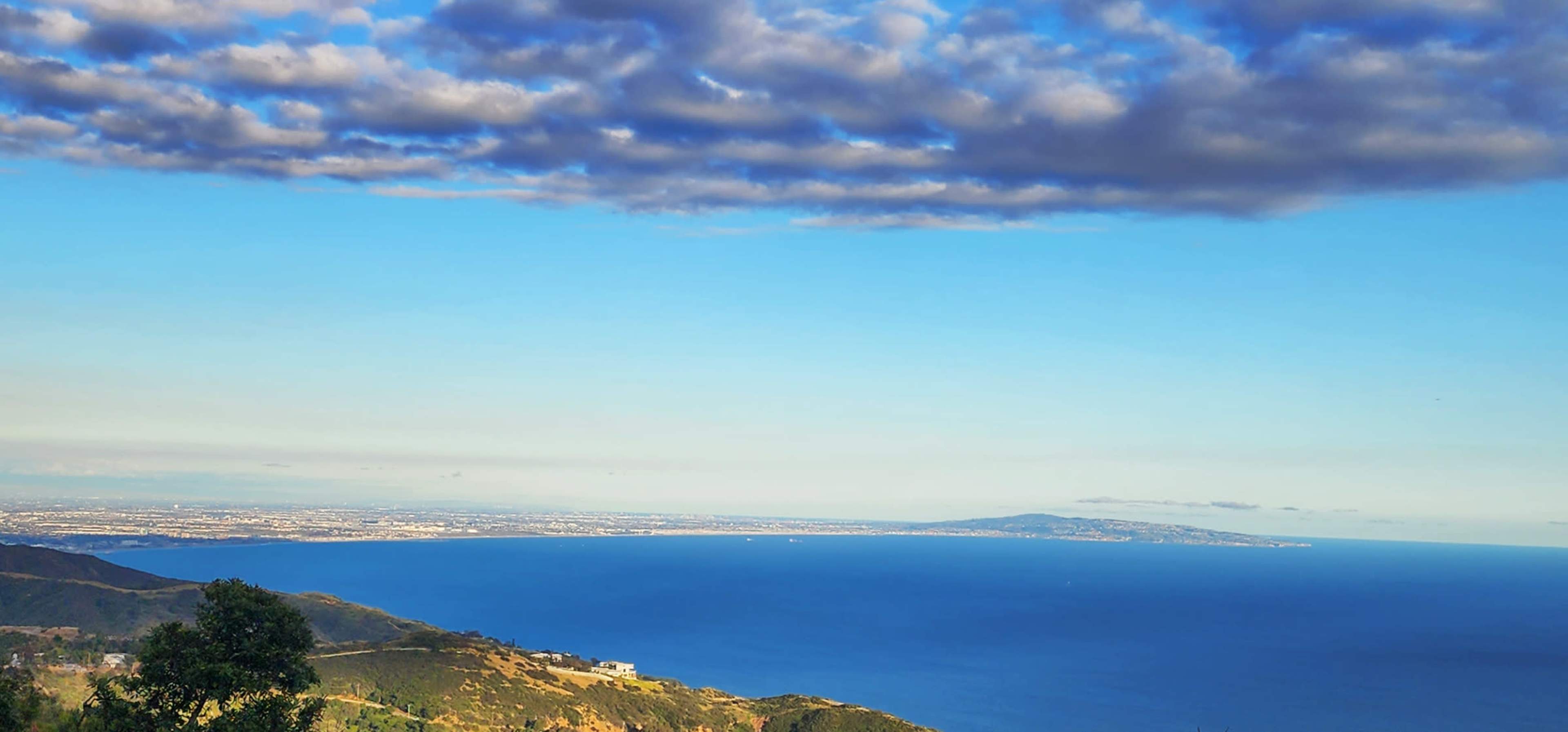 The image shows a coastal landscape with a view of the ocean, land, and a cloudy sky.