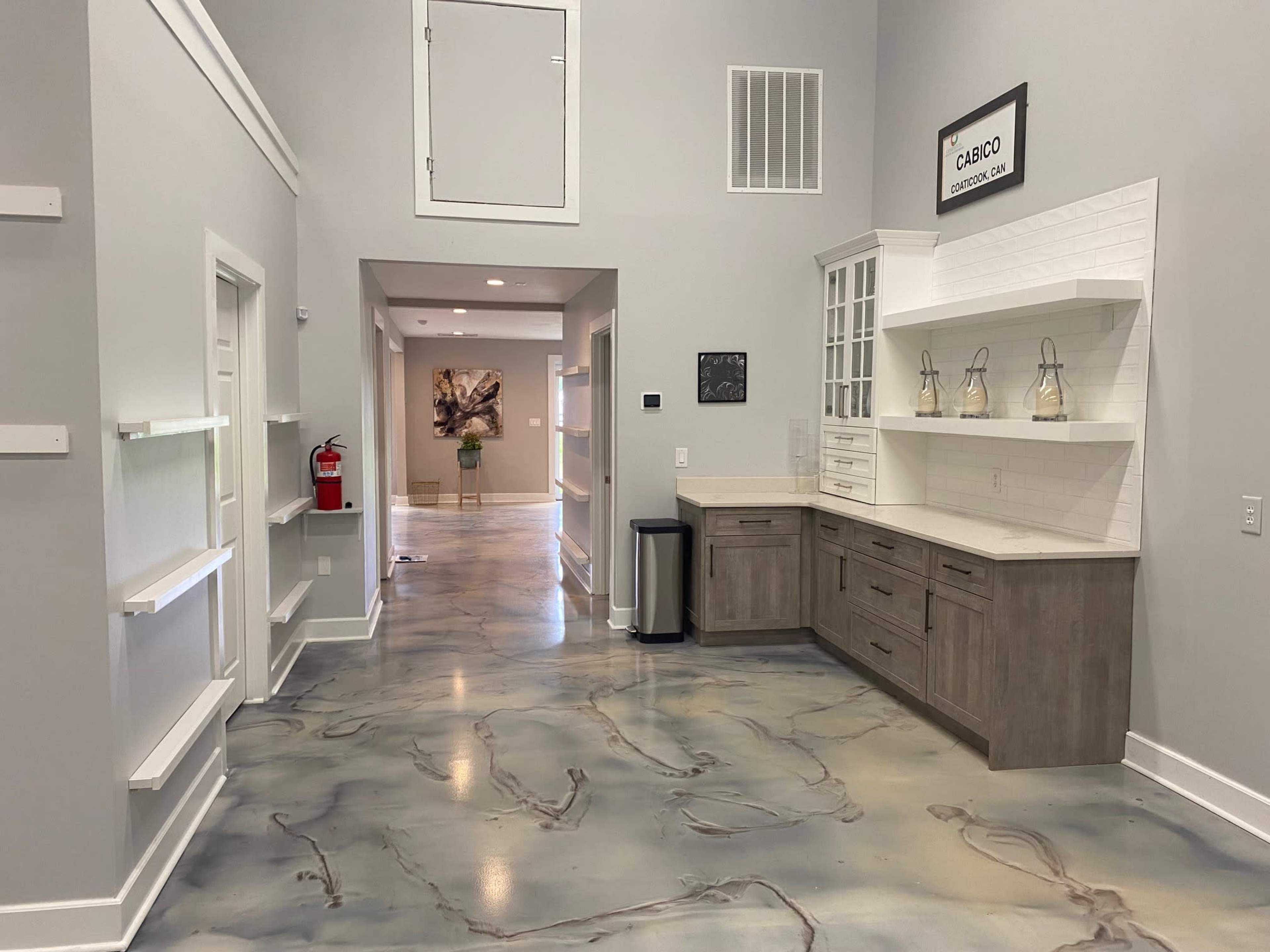 A spacious room with light gray walls, a polished concrete floor featuring a marbled design, and built-in cabinetry along one wall.