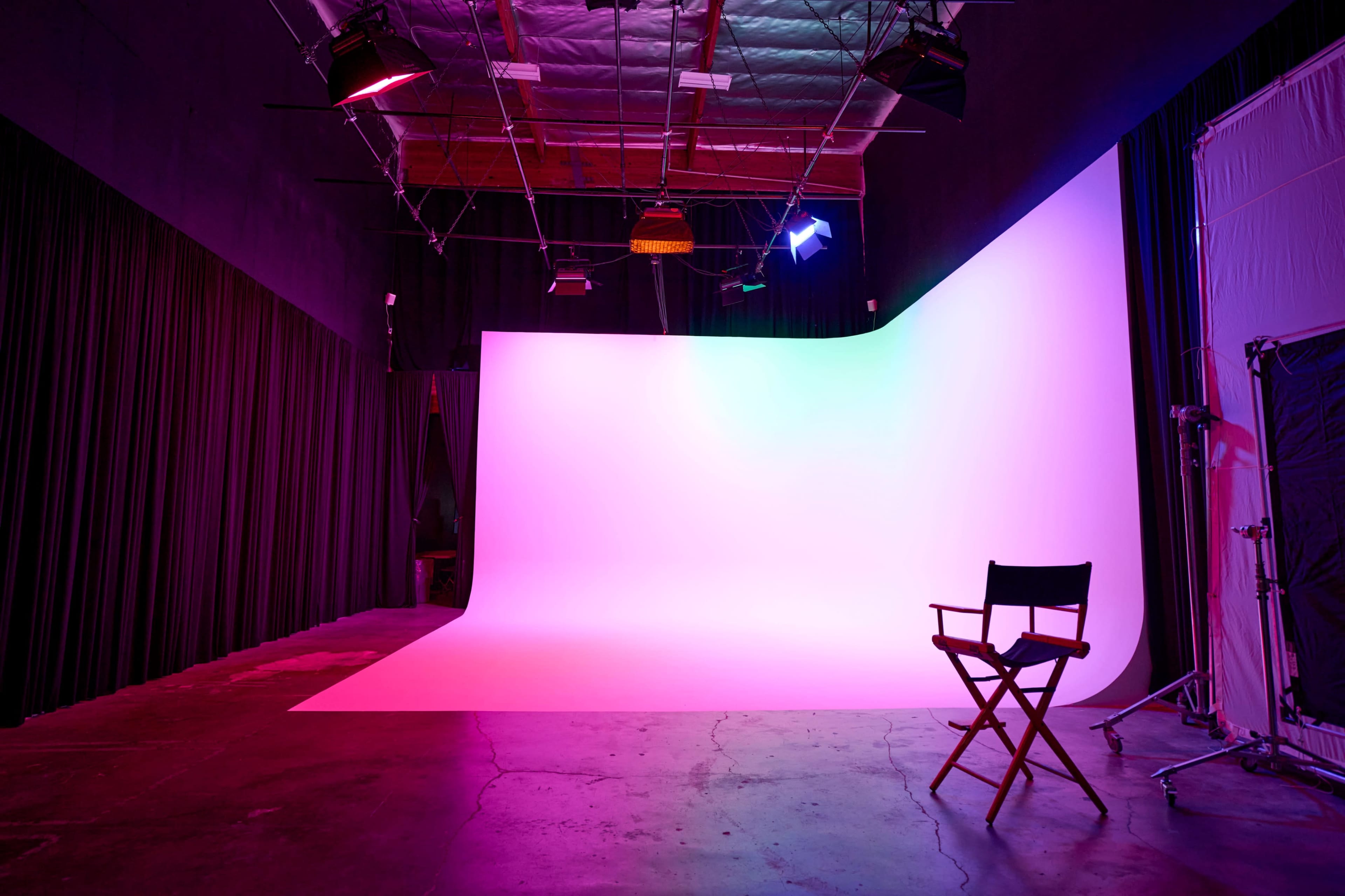 A photography studio featuring a blank backdrop with varying colored lights and a director's chair positioned on the floor.