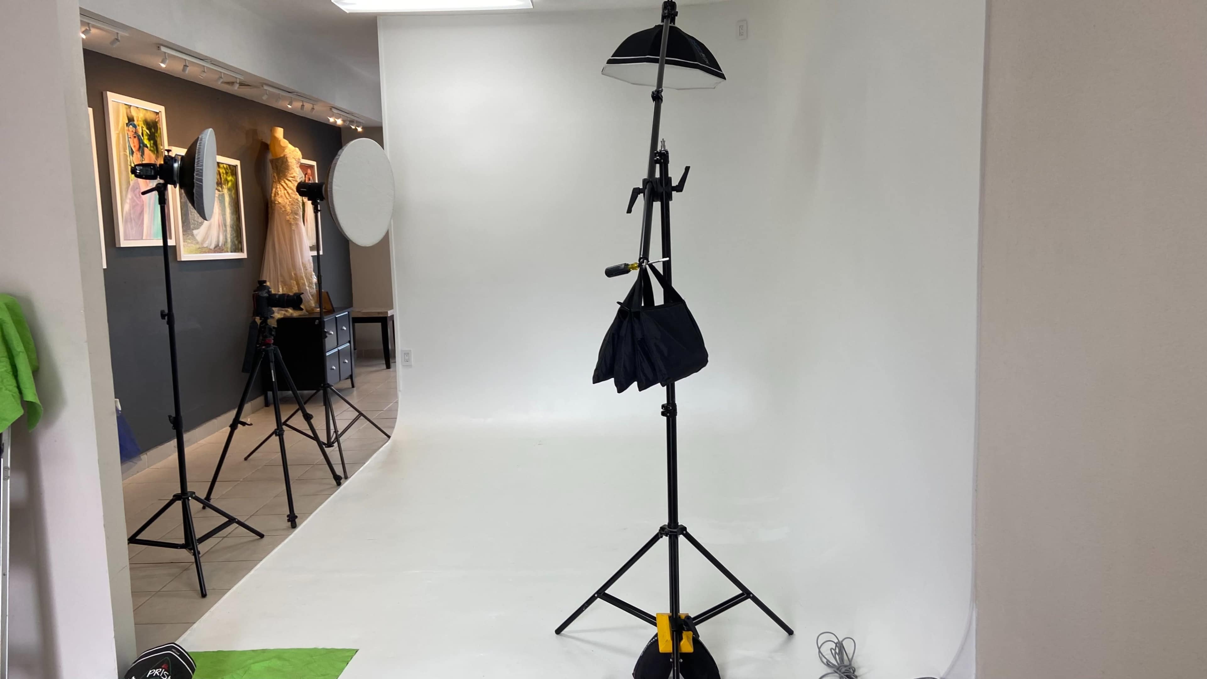 A photography studio with a blank white backdrop, softbox lights, and a tripod stand holding a reflector.