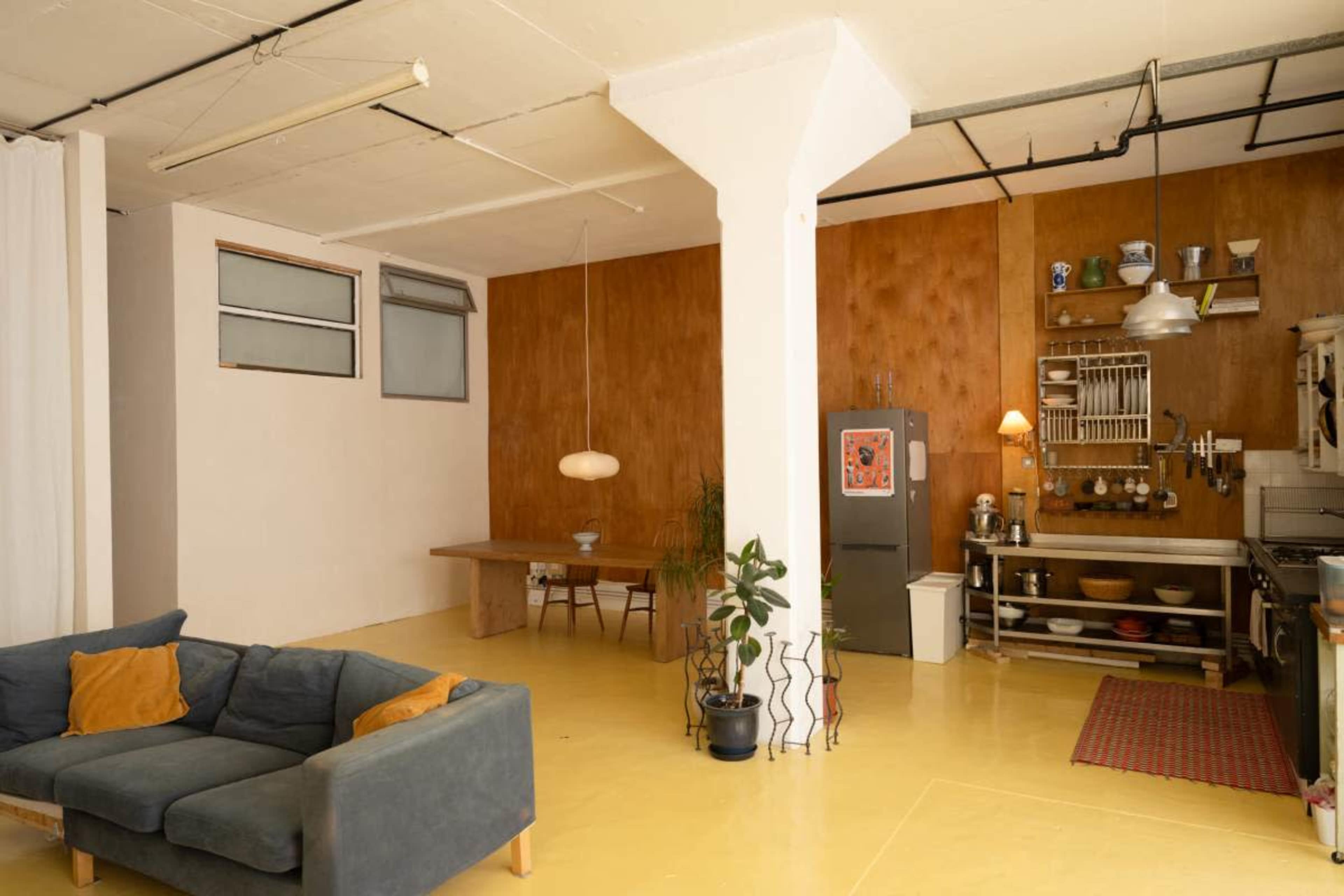 The image shows a spacious, modern interior featuring a living area with a couch, a dining table, and a kitchen area with various utensils and appliances.