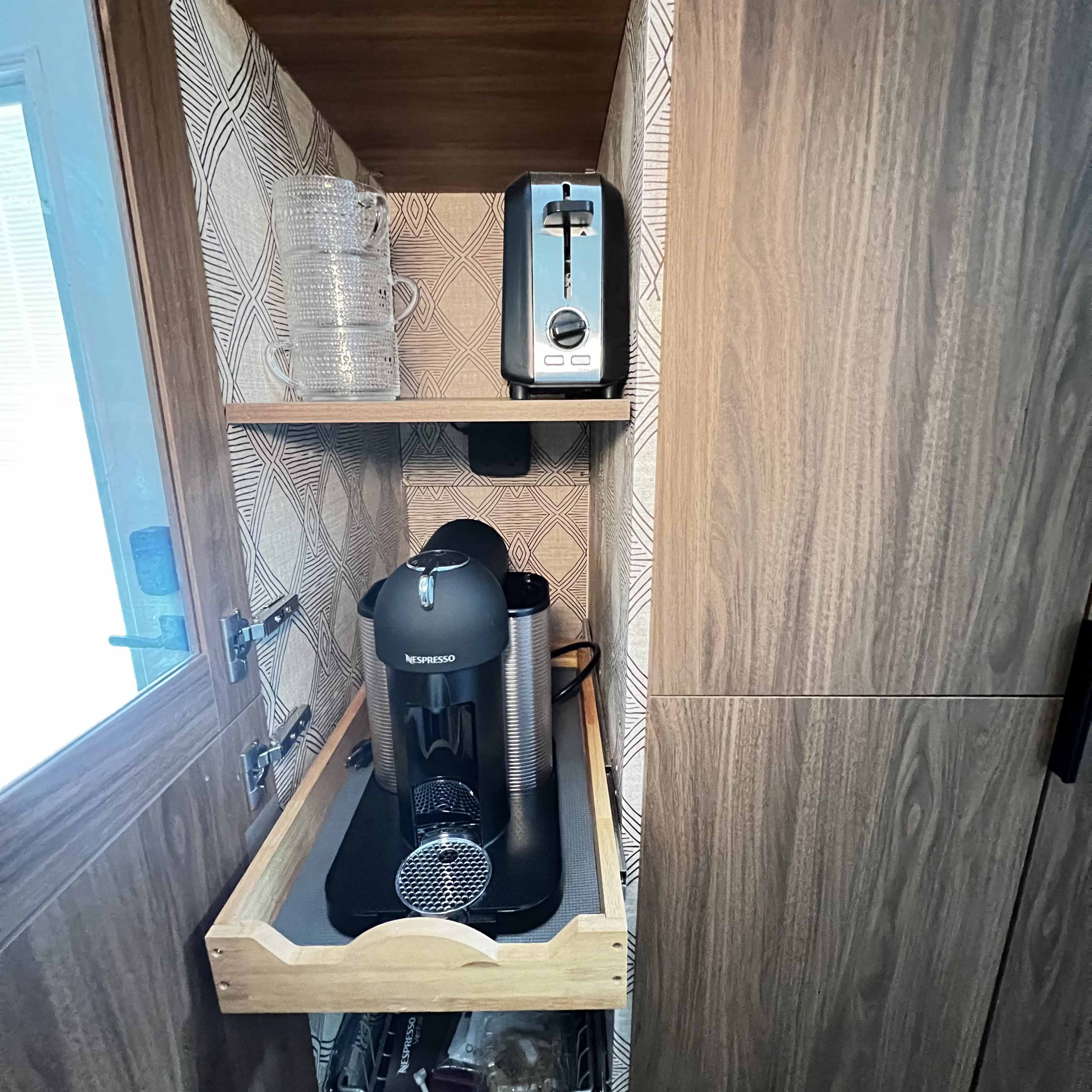 The image shows a wooden cabinet shelf containing a coffee maker, a toaster, and a couple of glass pitchers.