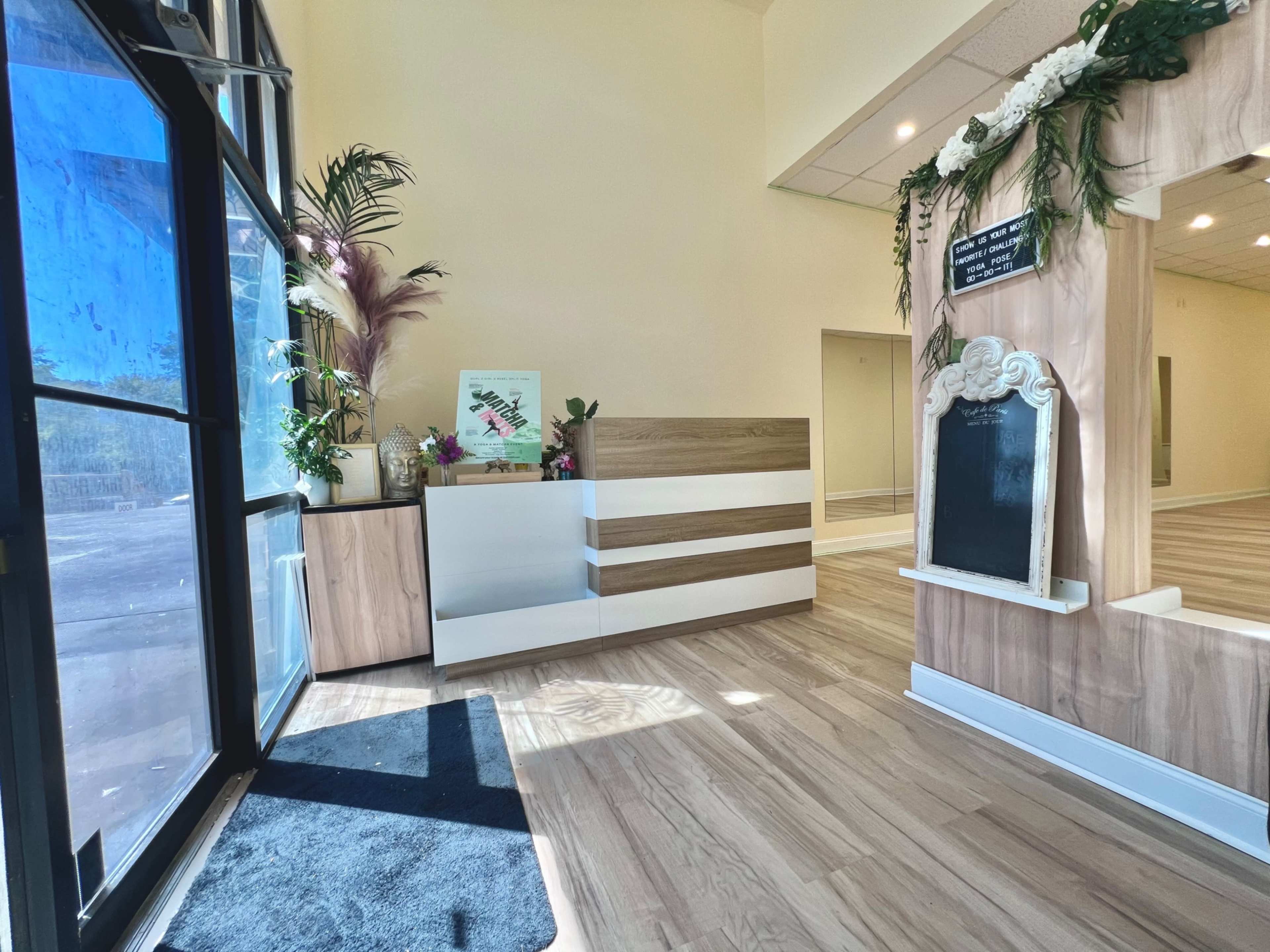 The image shows a bright, modern reception area featuring a sleek front desk, decorative plants, and a chalkboard element on the wall.